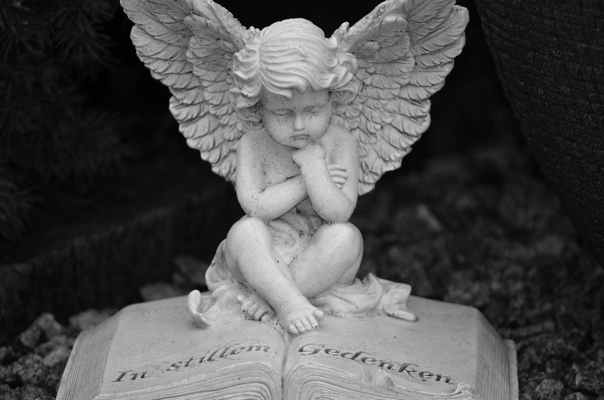 A black and white photo of a statue of an angel sitting on top of an open book.