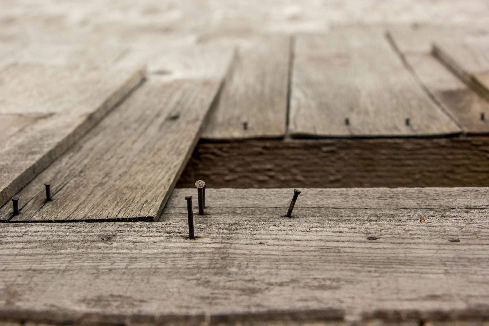 A close up of a wooden floor with nails sticking out of it.