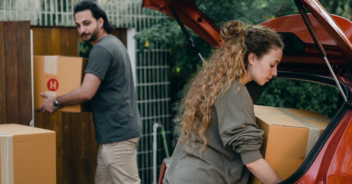 A man and a woman are loading boxes into the back of a car.