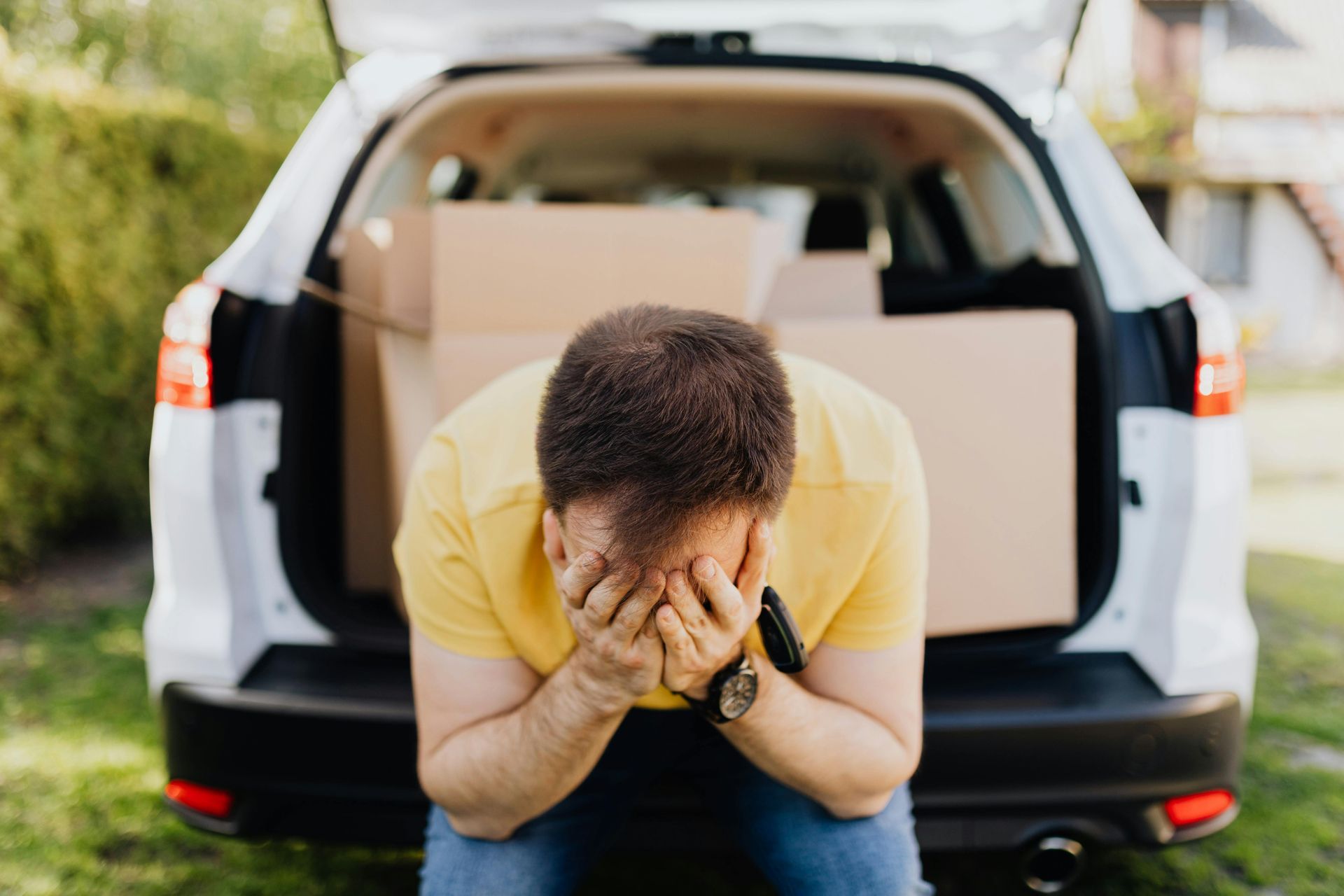 A man is bending down in front of a car with boxes in the back.