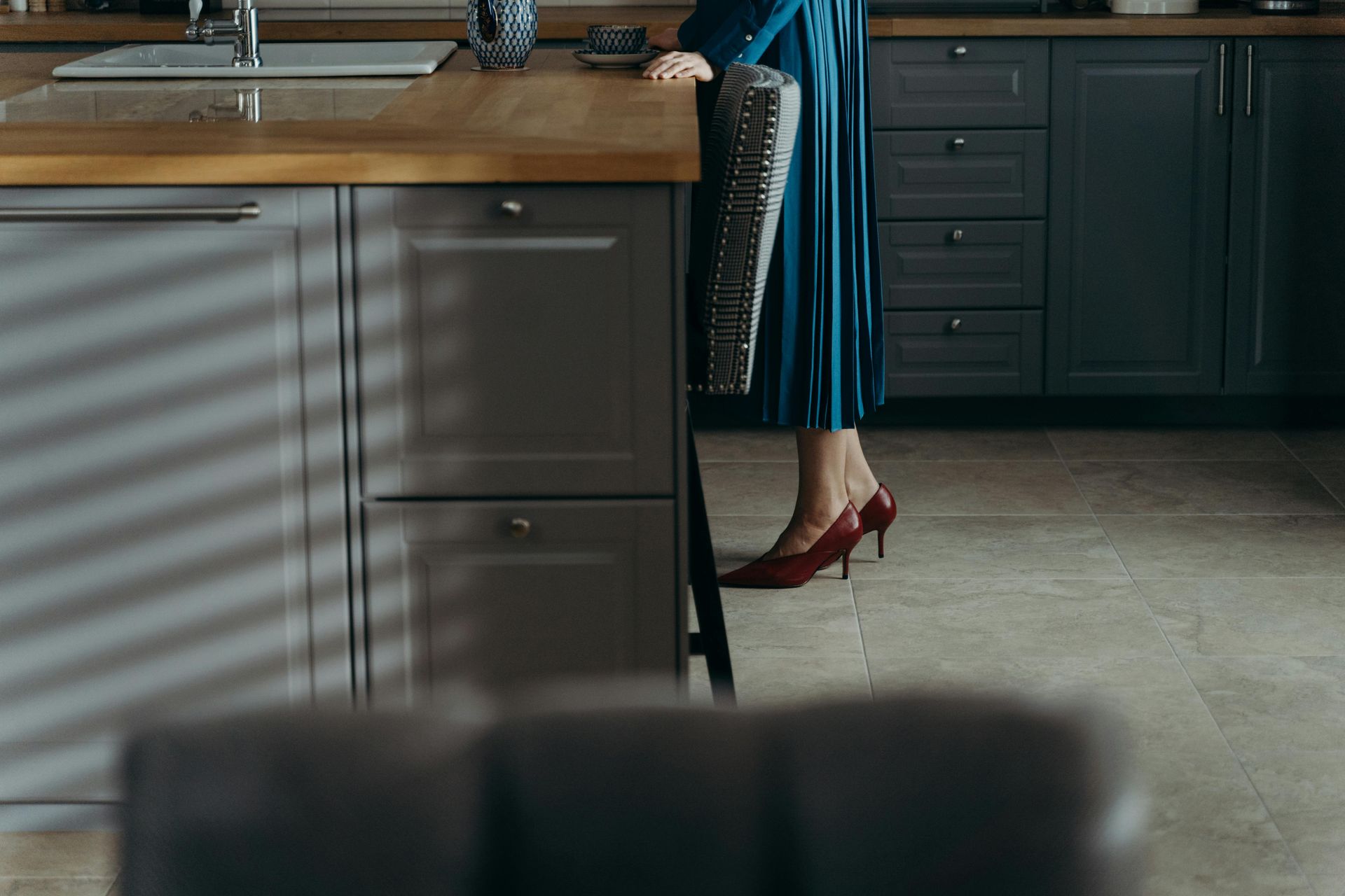 A woman in a blue dress and red heels is standing in a kitchen.