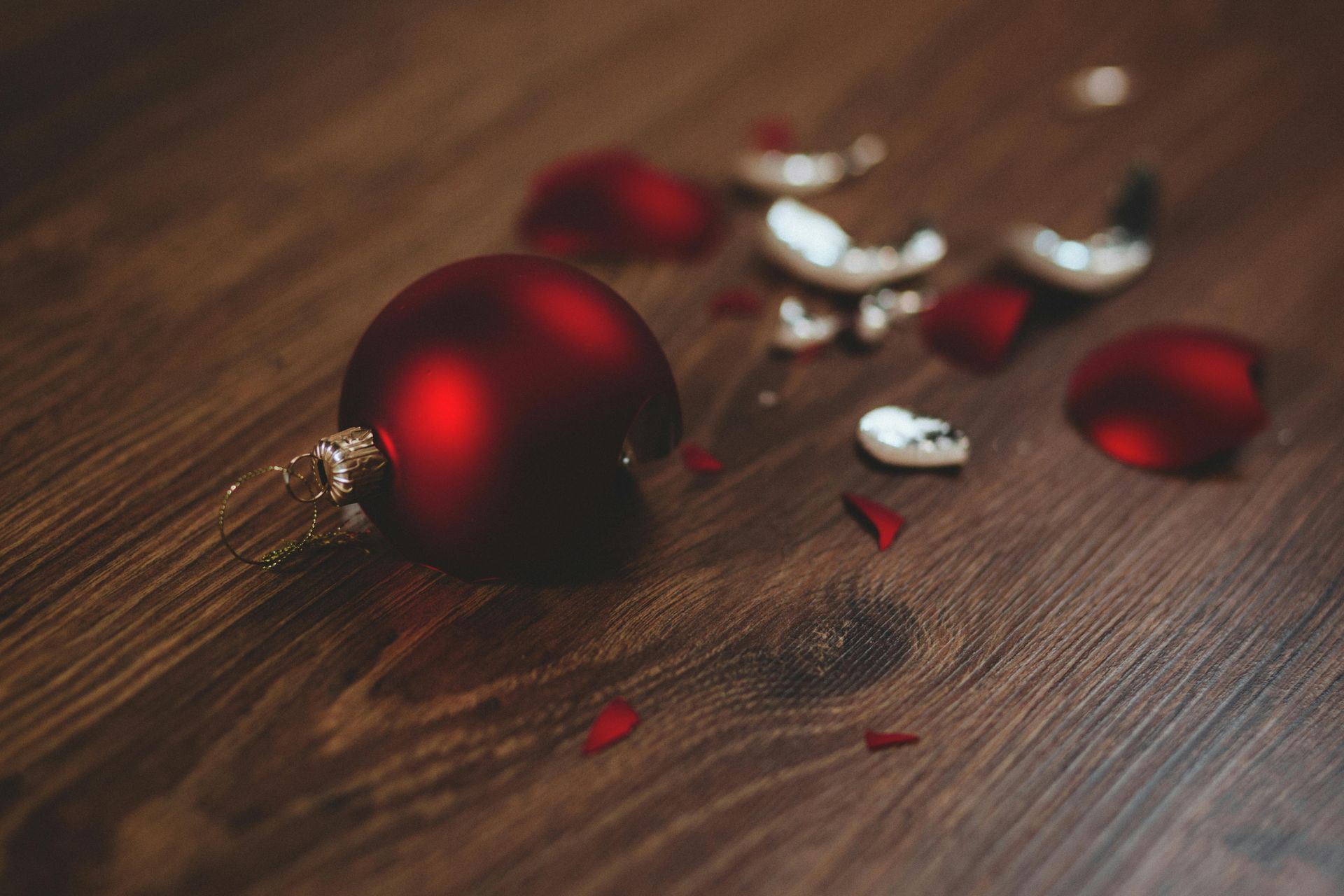 A broken red christmas ornament is laying on a wooden table.