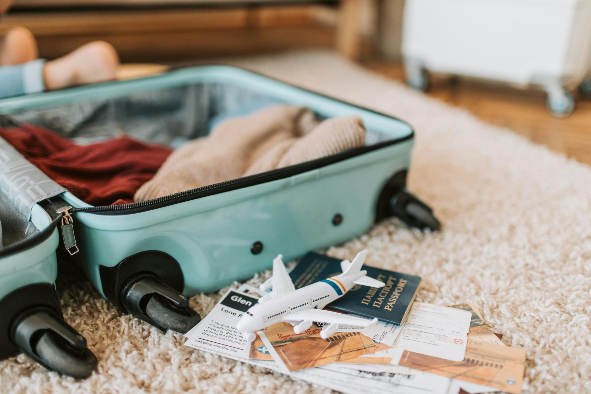 Open blue suitcase with clothes, airplane model, and travel documents on a fluffy rug.