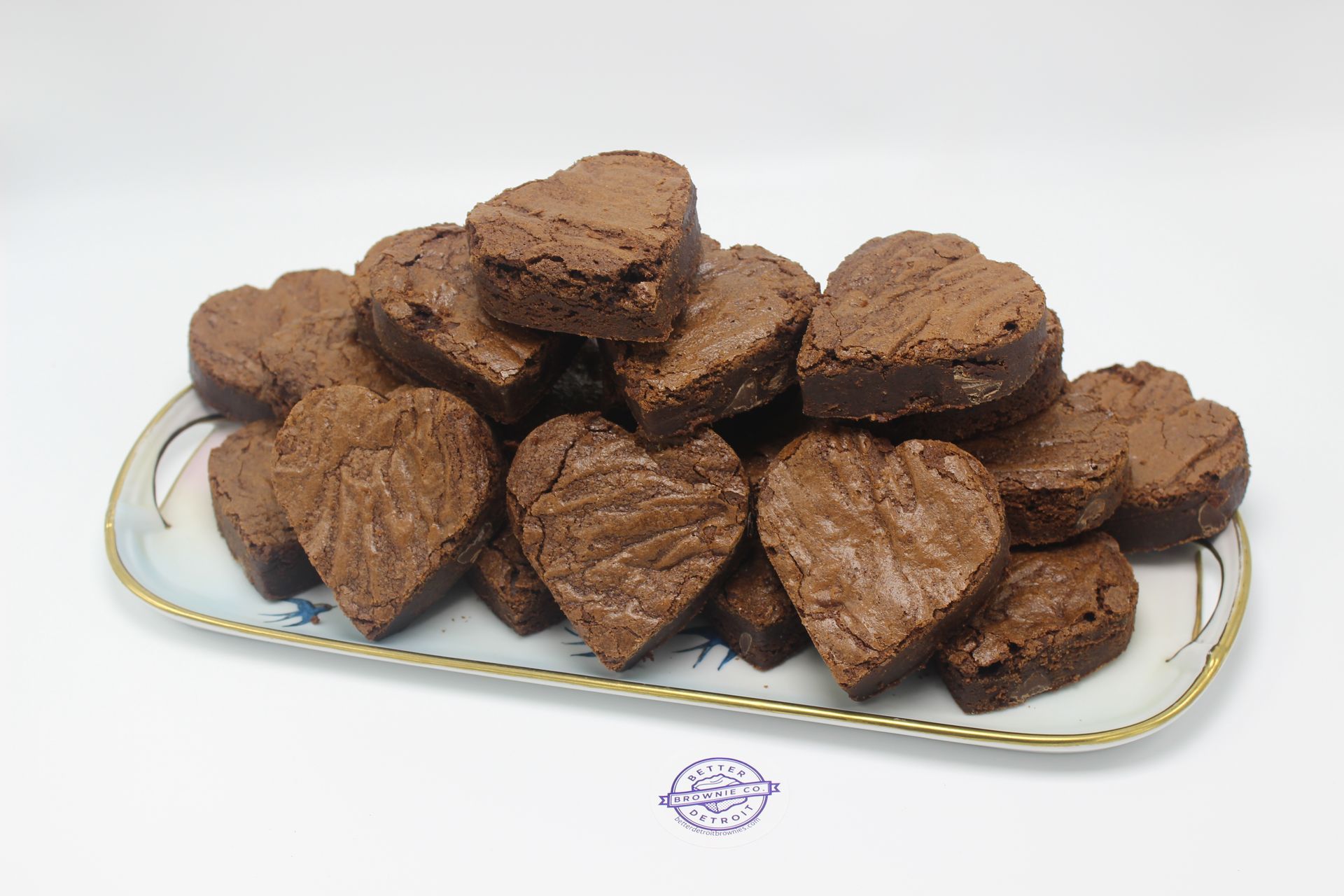 Heart-shaped chocolate brownies on a decorative platter, piled high, against a white background.