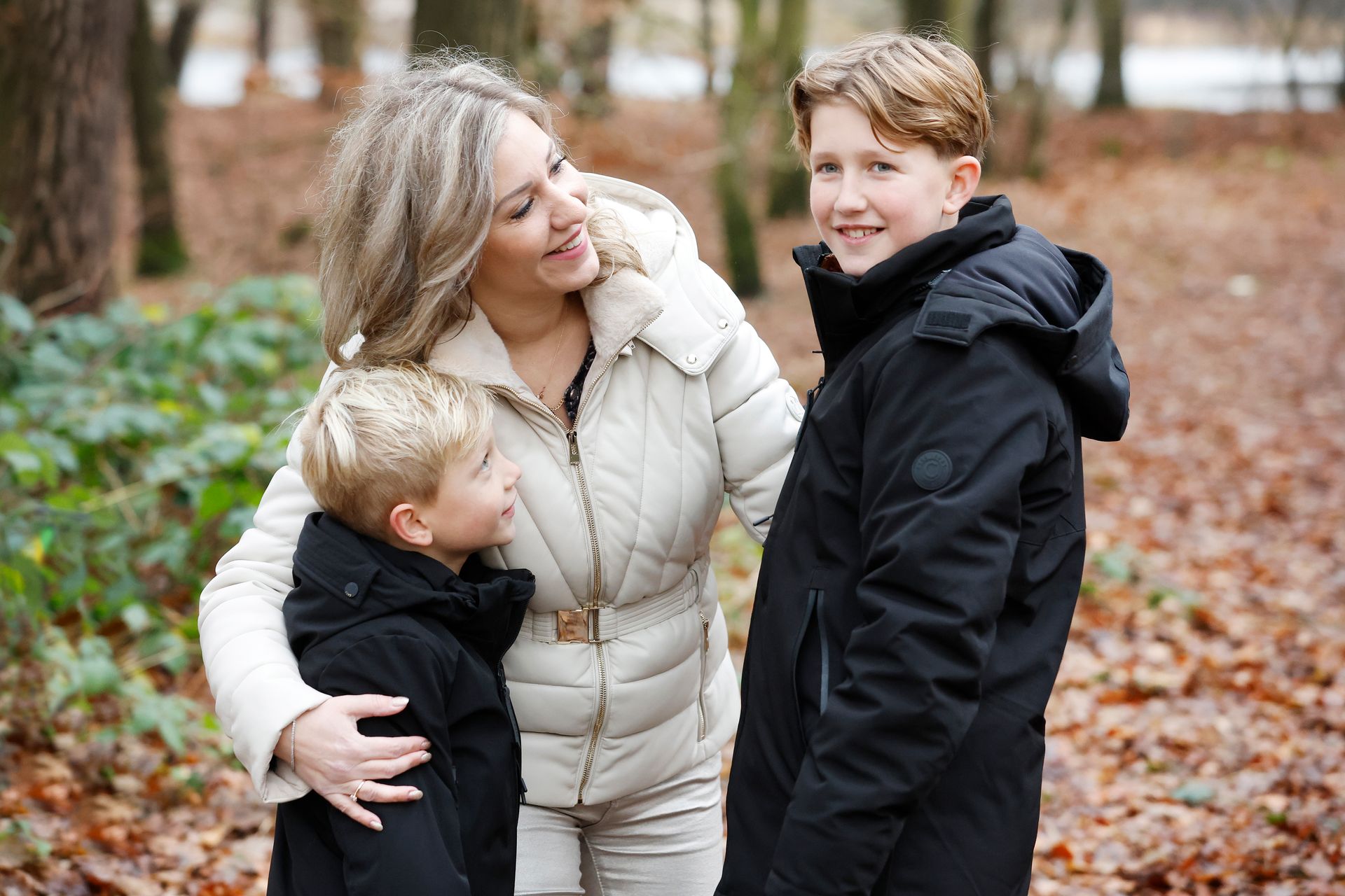 Een vrouw staat naast twee jongens in het bos.