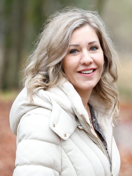 Een vrouw in een wit jasje lacht naar de camera.