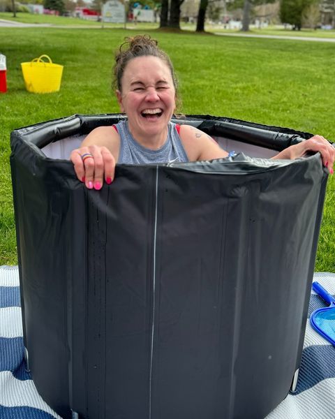 A woman is laughing while sitting in a bucket of water.