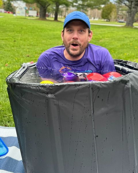 A man is sitting in a trash can filled with water.
