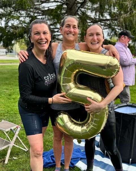 Three women are posing for a picture while holding a balloon in the shape of a number five.