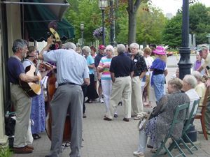 A group of people are gathered on a sidewalk with a man playing a guitar