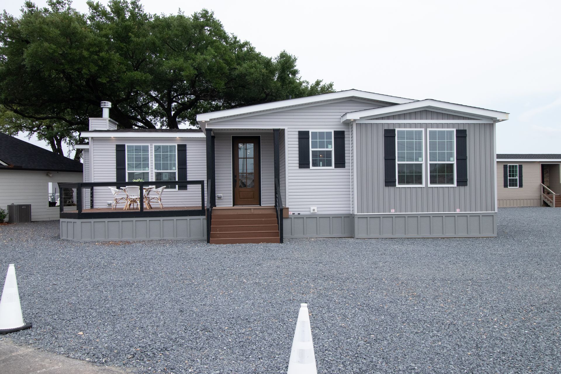 Gray manufactured home with a small porch and gravel lot under overcast skies