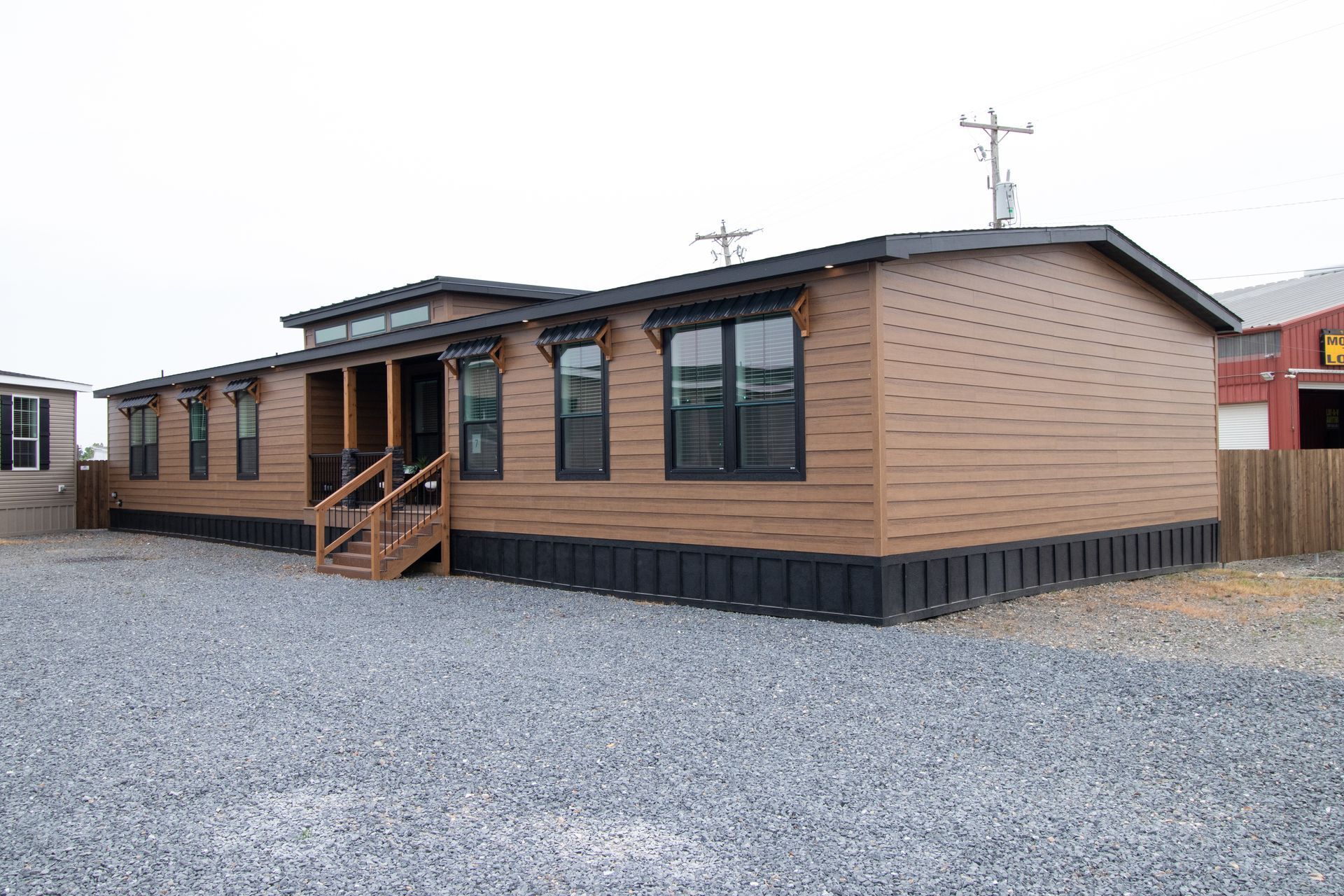 Single-story tan modular building with black shutters, small porch, and gravel lot