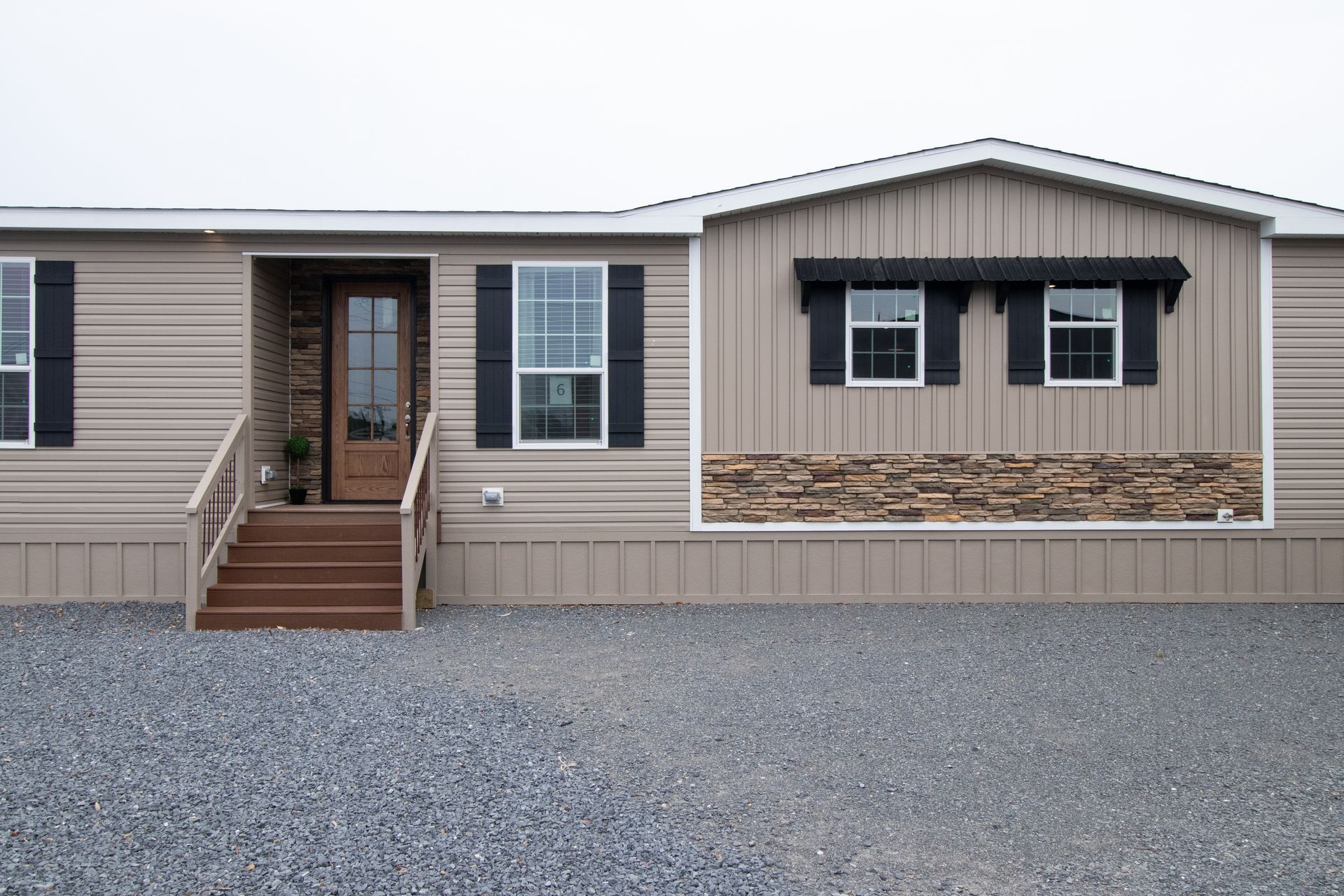 Front view of a tan mobile home with a small porch and gravel driveway.