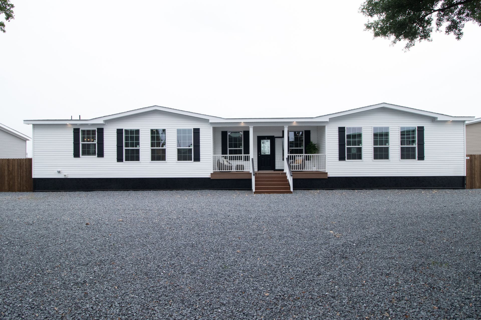 White single-story house with dark shutters, front steps, and a large gravel driveway