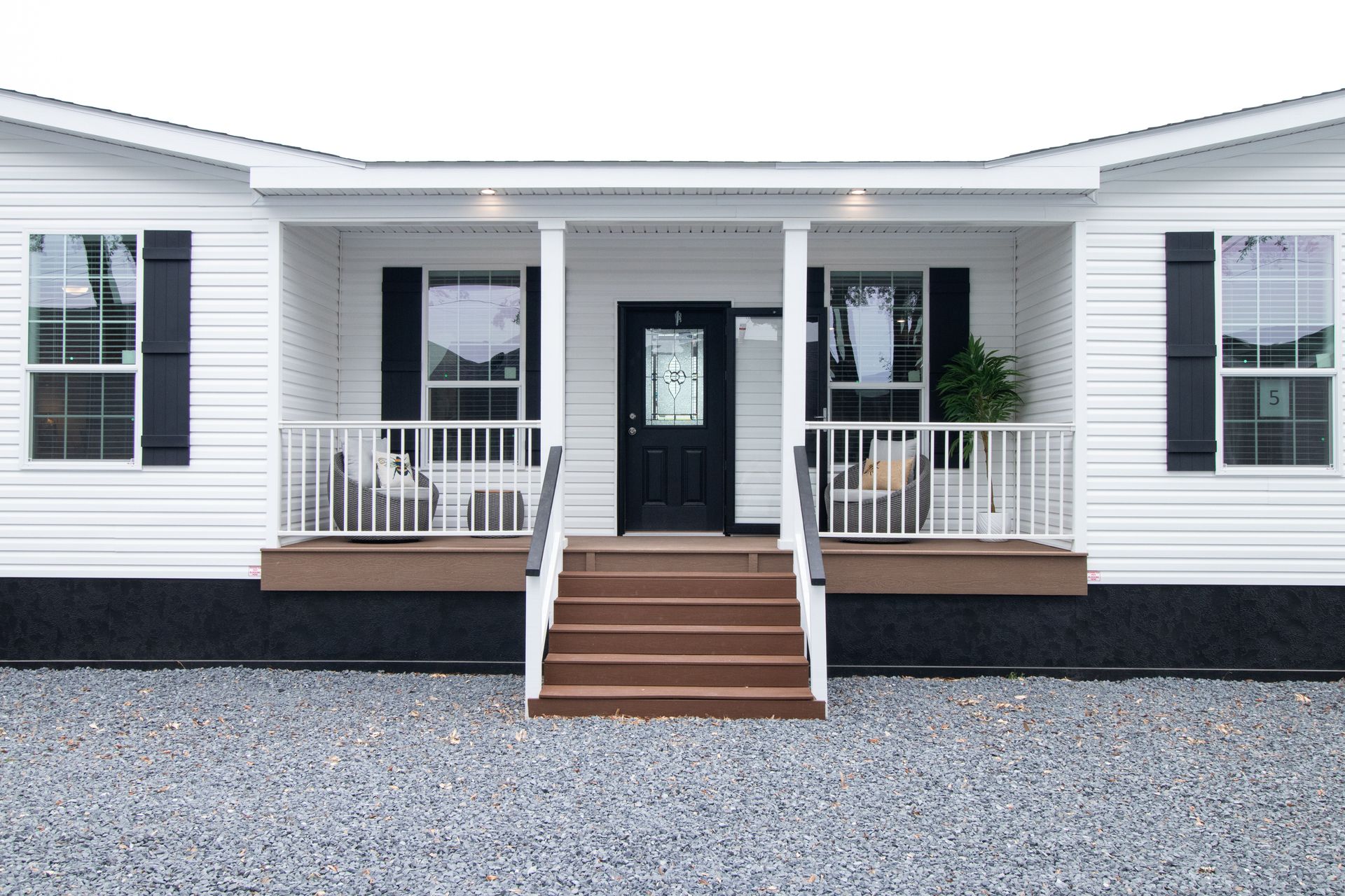 White house front with central steps, porch railings, black shutters, and a gravel driveway