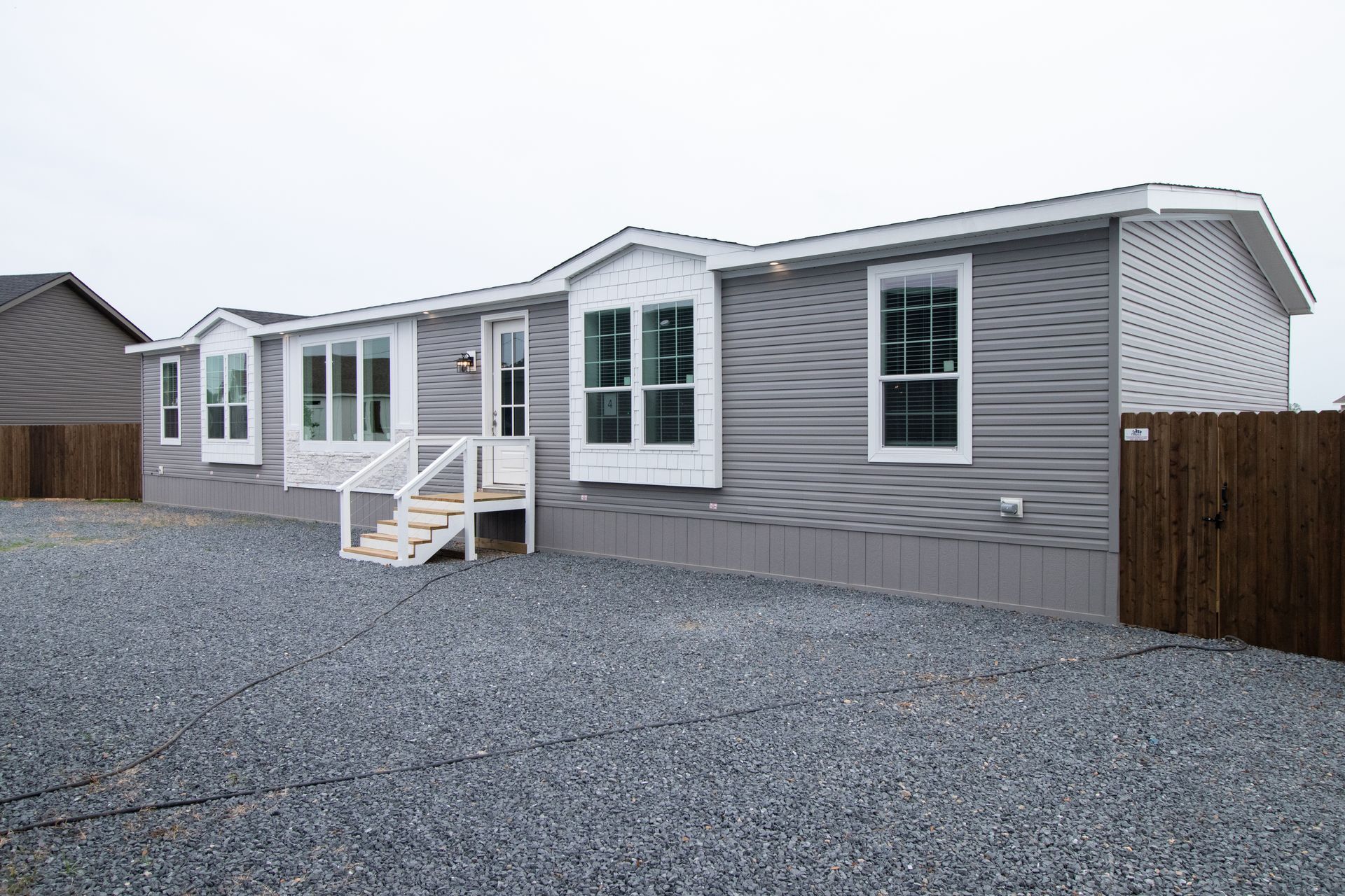 Gray manufactured home with white trim and small front steps on a gravel lot