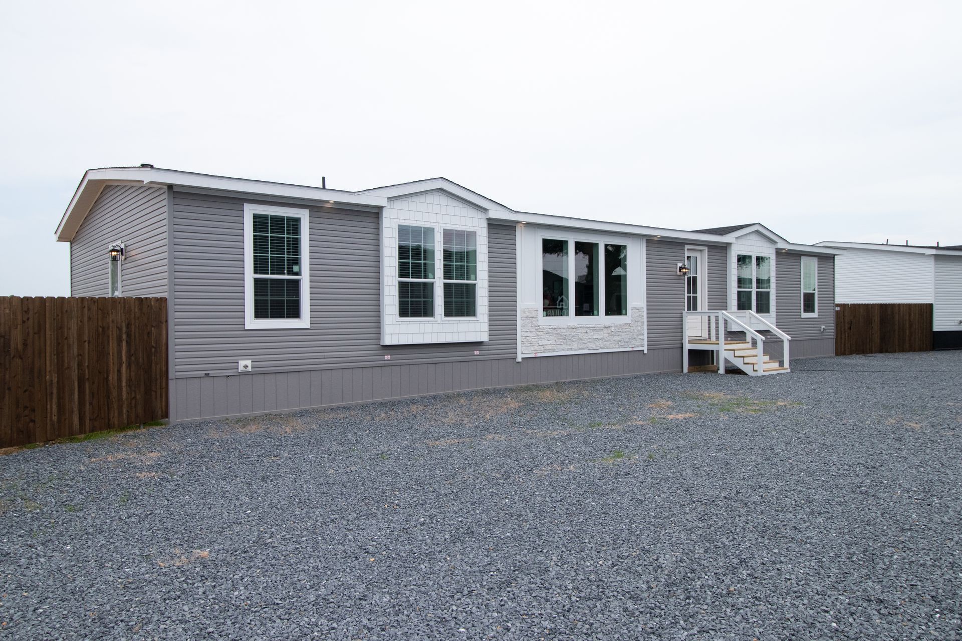 Gray manufactured home with white trim and a small front porch on a gravel lot
