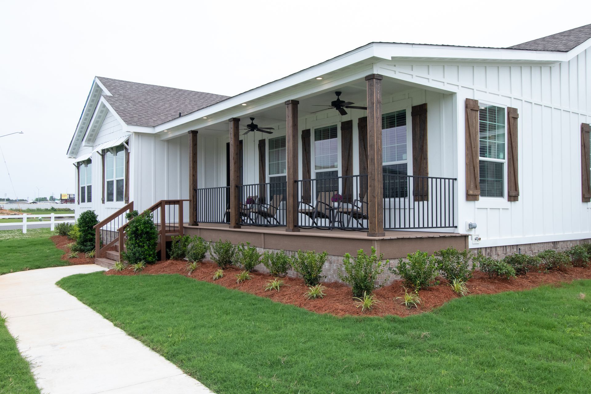White farmhouse with front porch, dark shutters, and green lawn beside a sidewalk