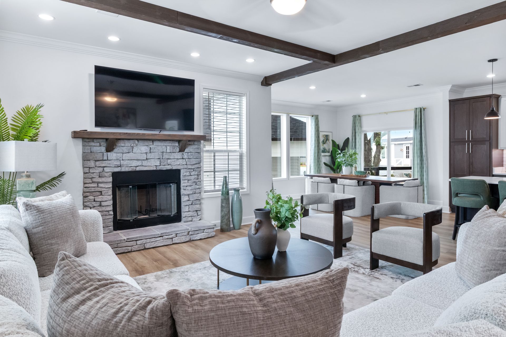 Bright modern living room with white sofas, stone fireplace, TV, and round coffee table