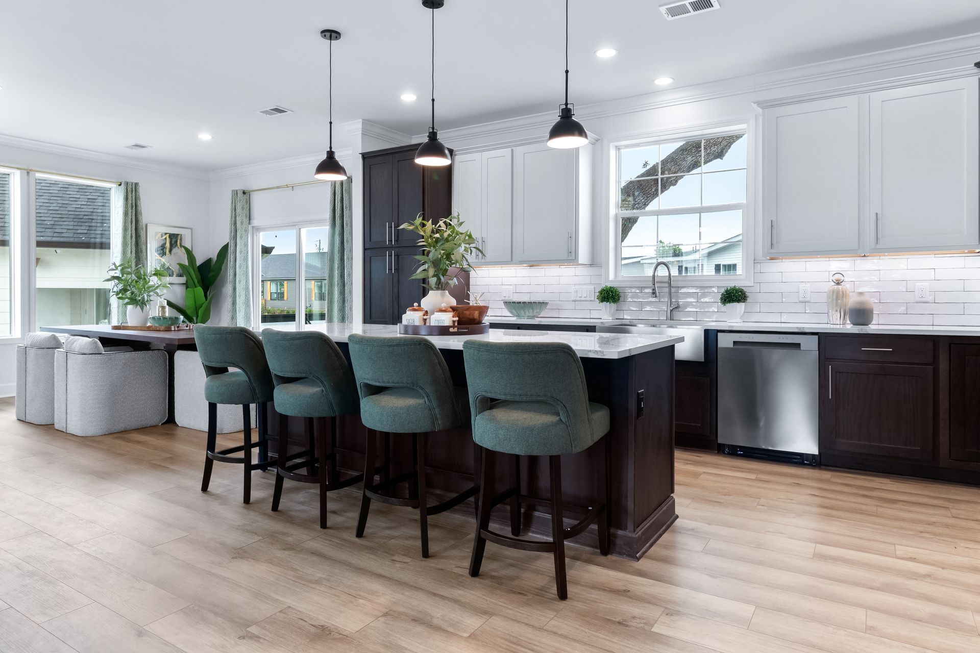 Modern open kitchen with dark island, teal stools, pendant lights, and white cabinets