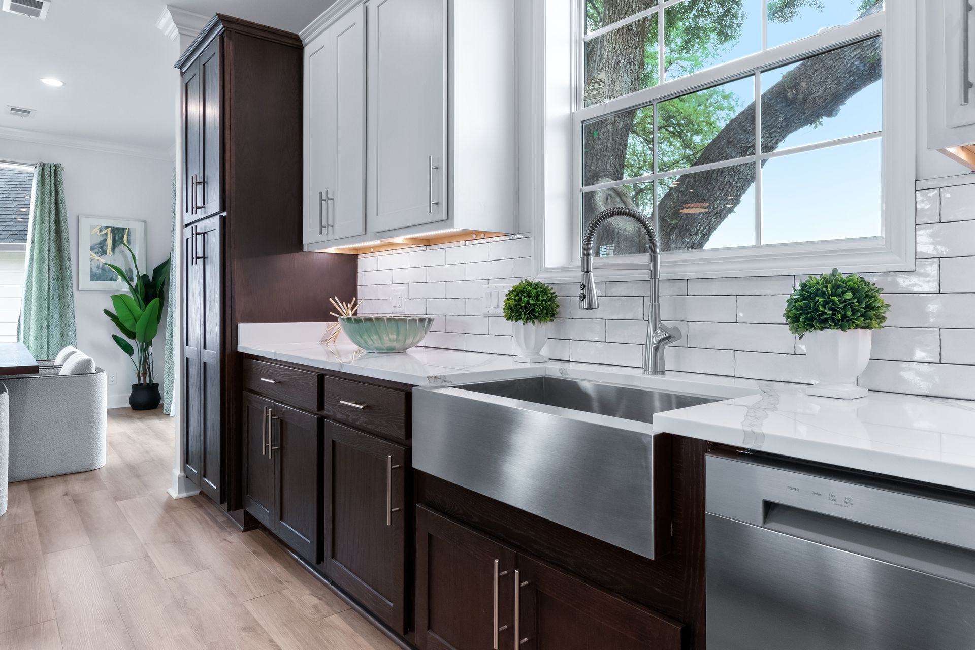 Modern kitchen with dark cabinets, white marble countertops, stainless sink, and large window.
