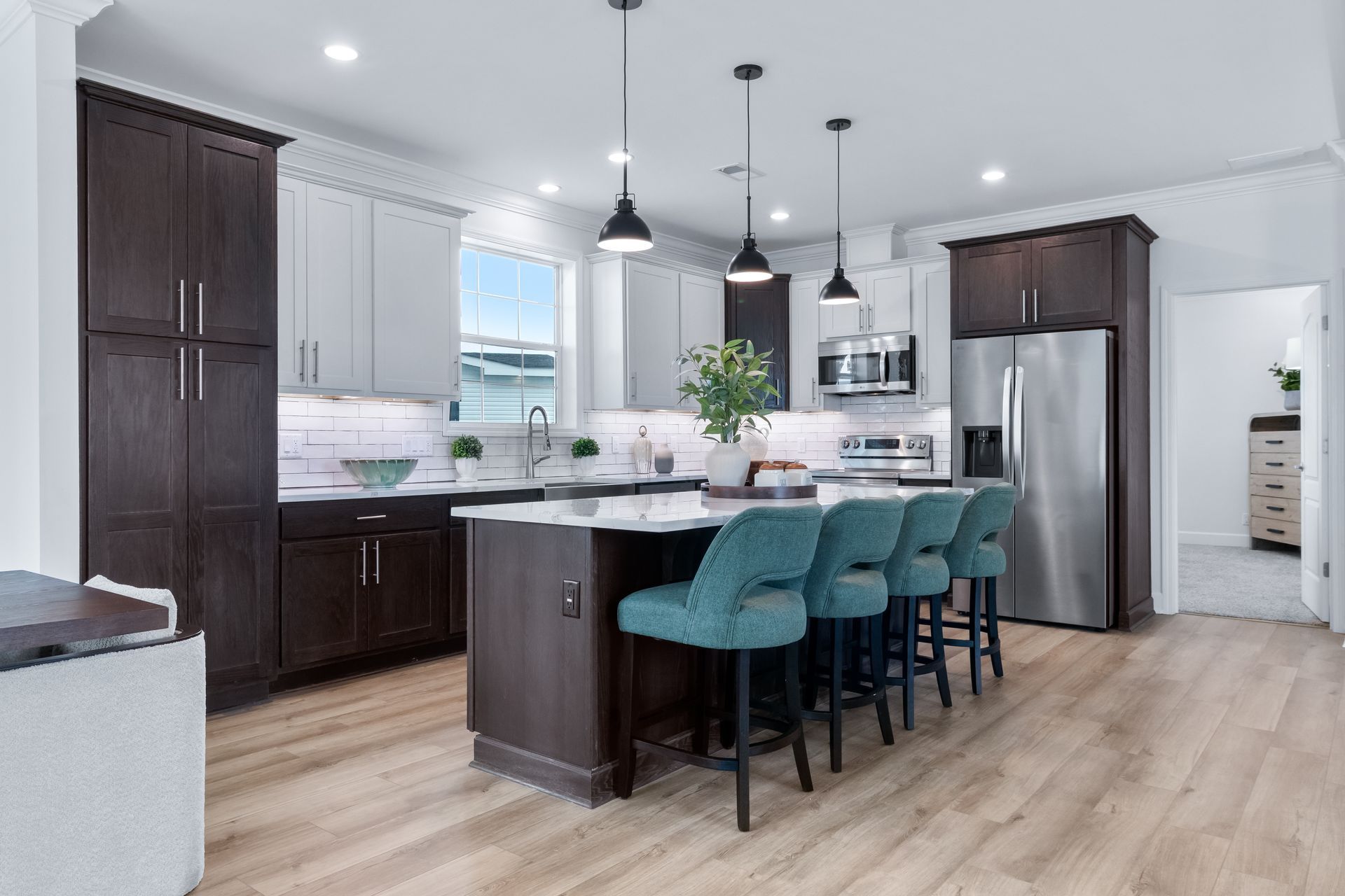 Modern white kitchen with dark wood cabinets, stainless appliances, island seating, and pendant lights