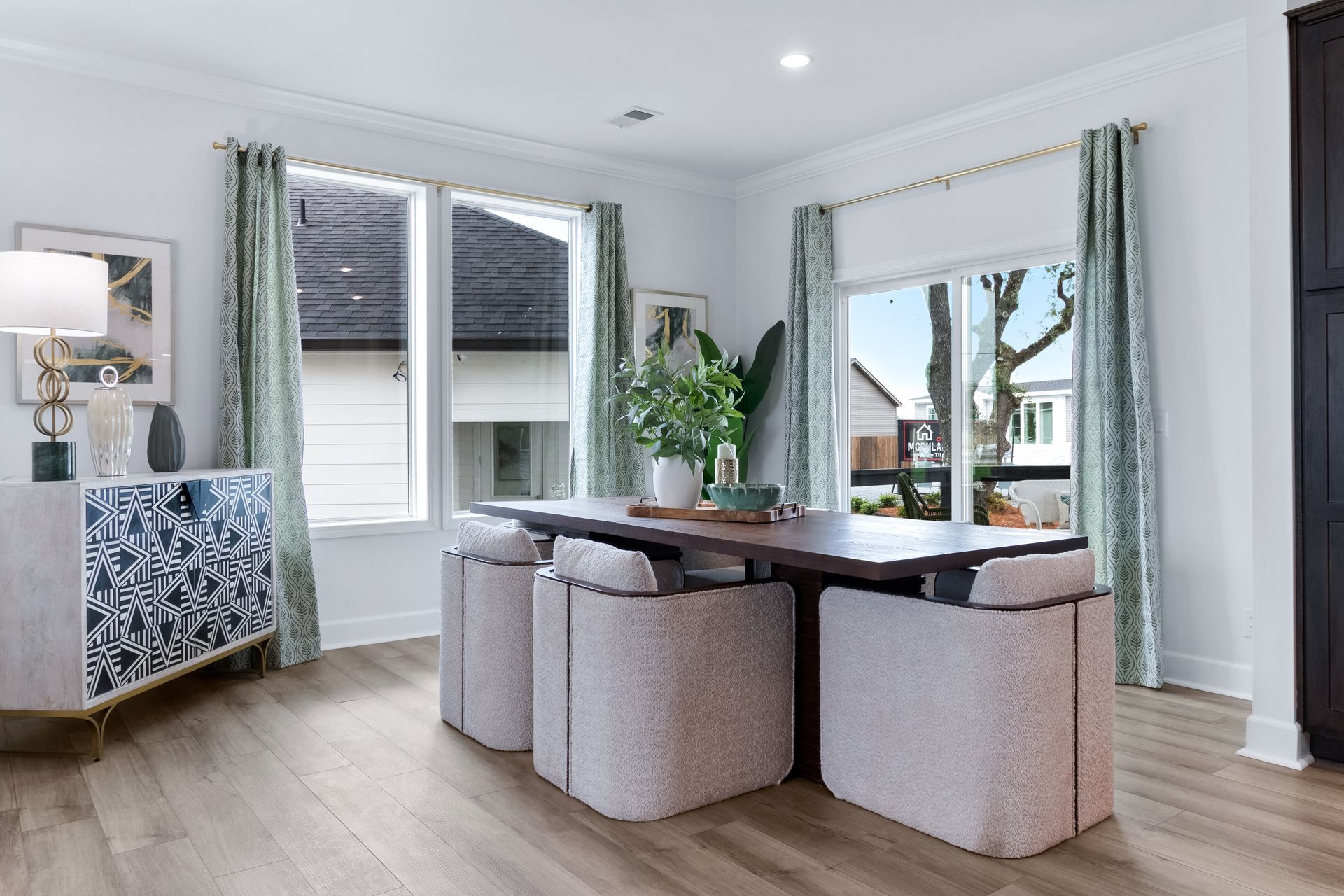 Bright dining room with a wooden table, woven chairs, large windows, and a blue patterned sideboard.