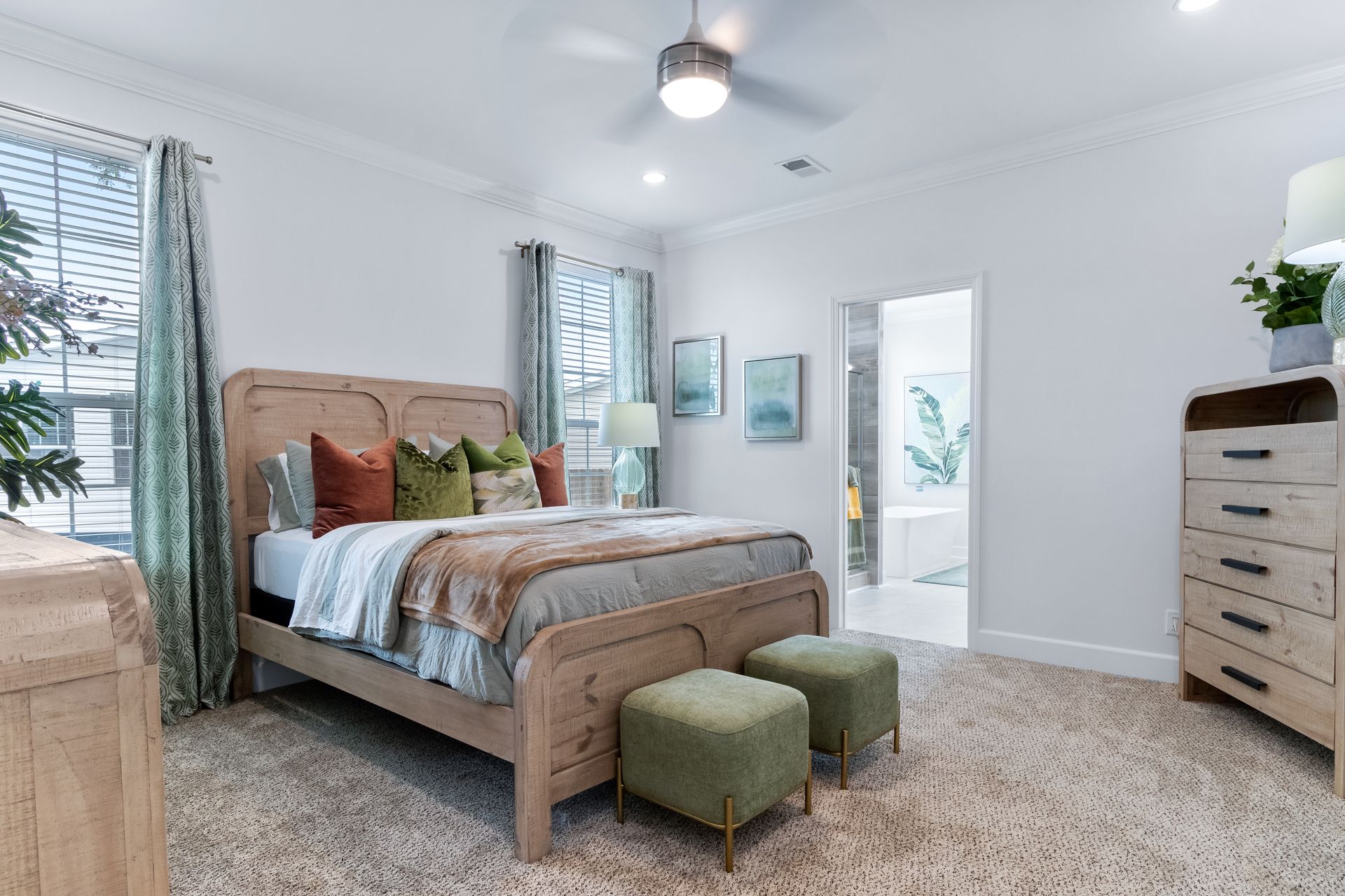 Bright bedroom with tan bed, green ottomans, white walls, and dresser by a window