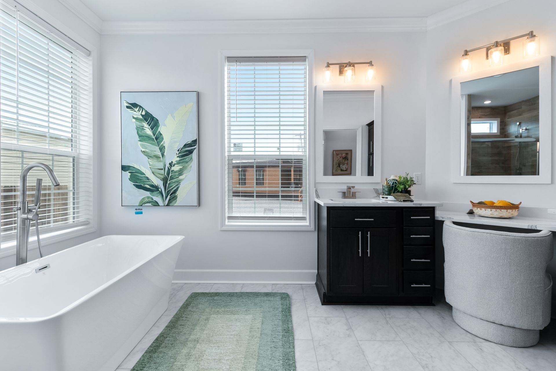 Bright white bathroom with freestanding tub, double vanity, large windows, and green rug.