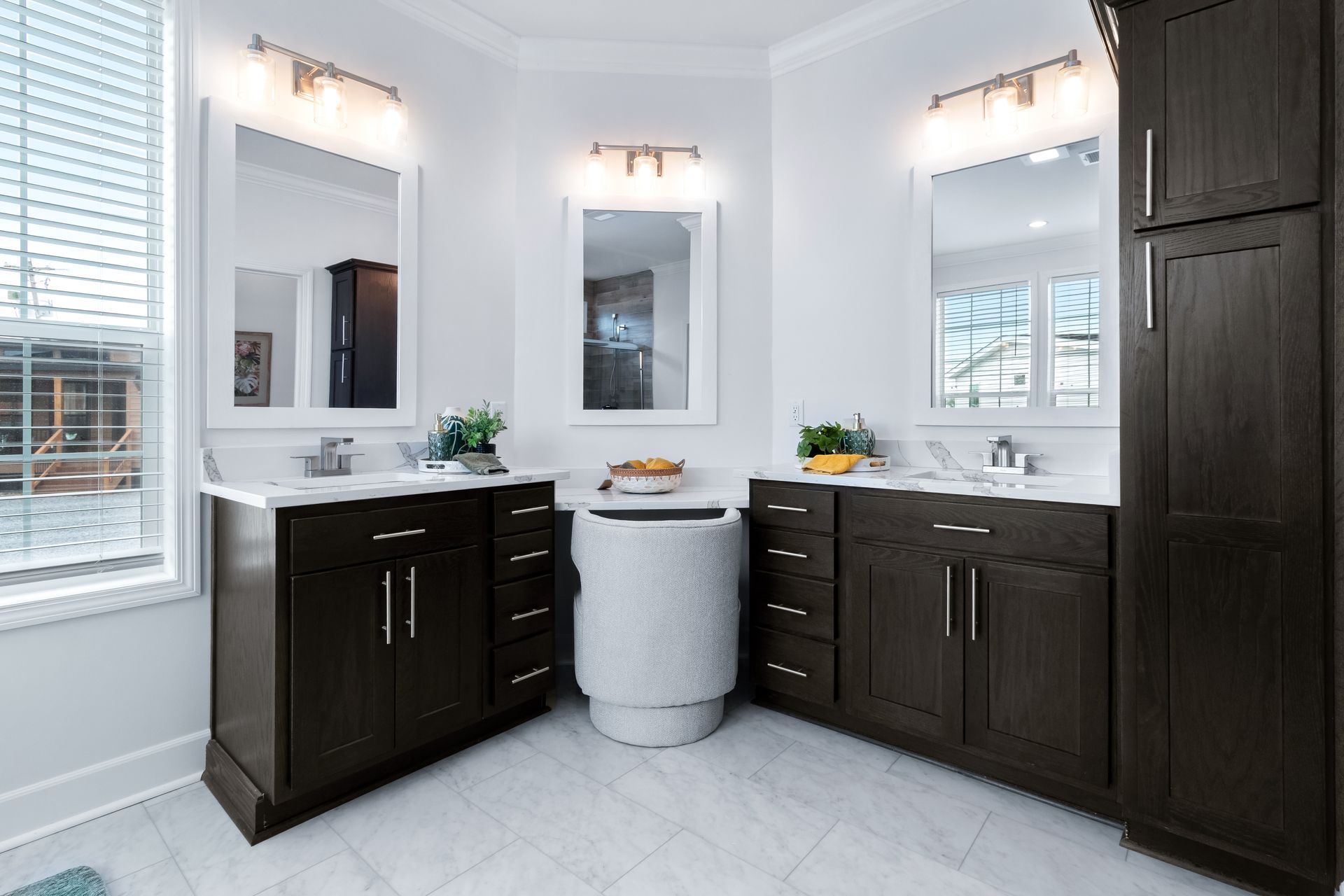 Modern bathroom vanity area with dark wood cabinets, white countertops, mirrors, and wall sconces