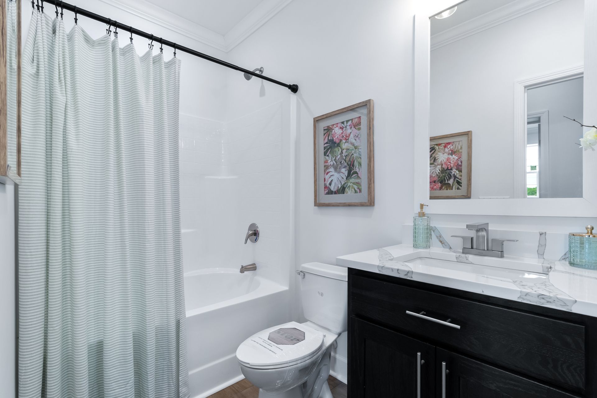 Bright white bathroom with bathtub, shower curtain, toilet, and vanity with mirror.