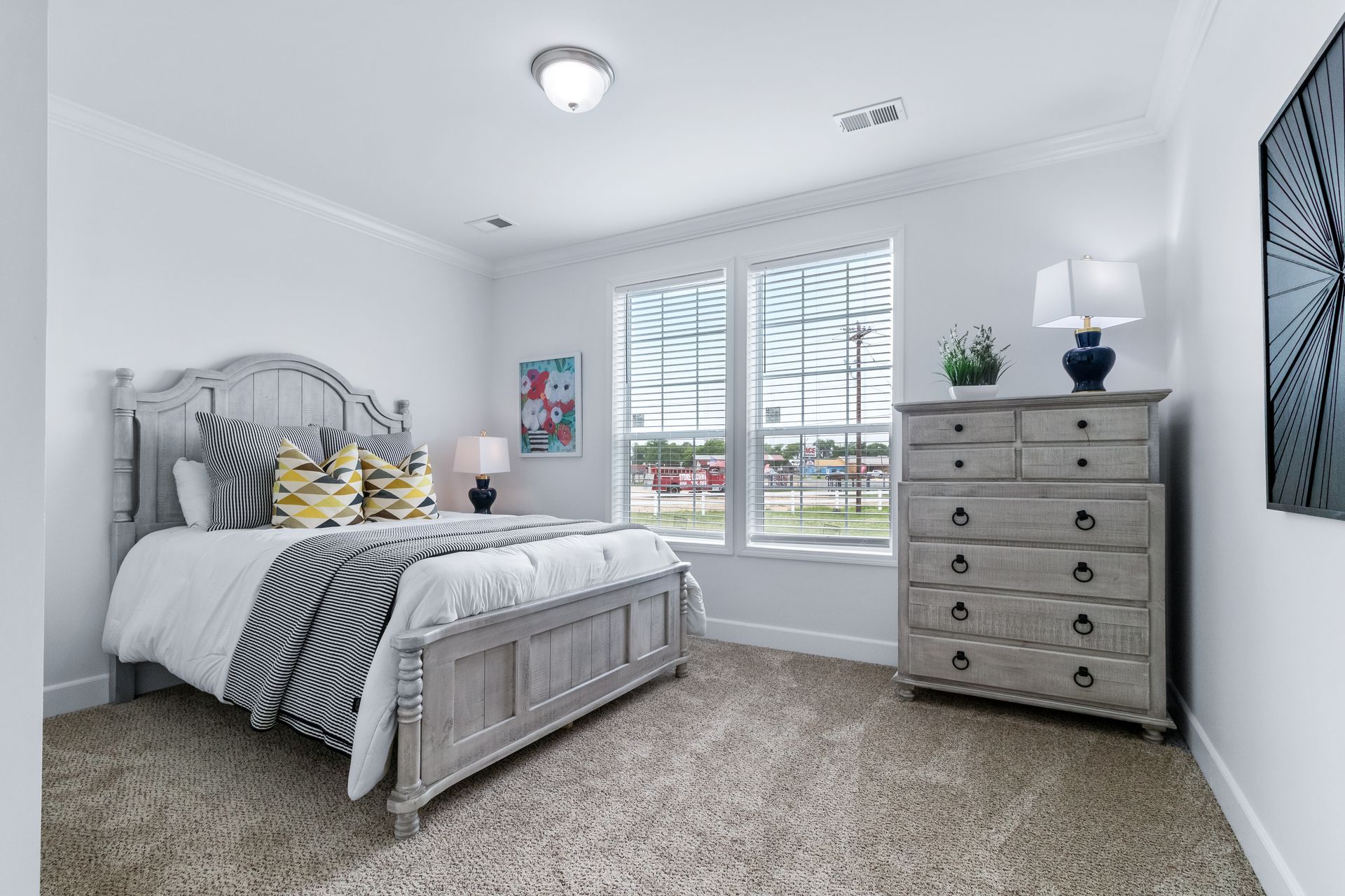 Bright bedroom with white bed, striped bedding, dresser, lamp, and window shutters