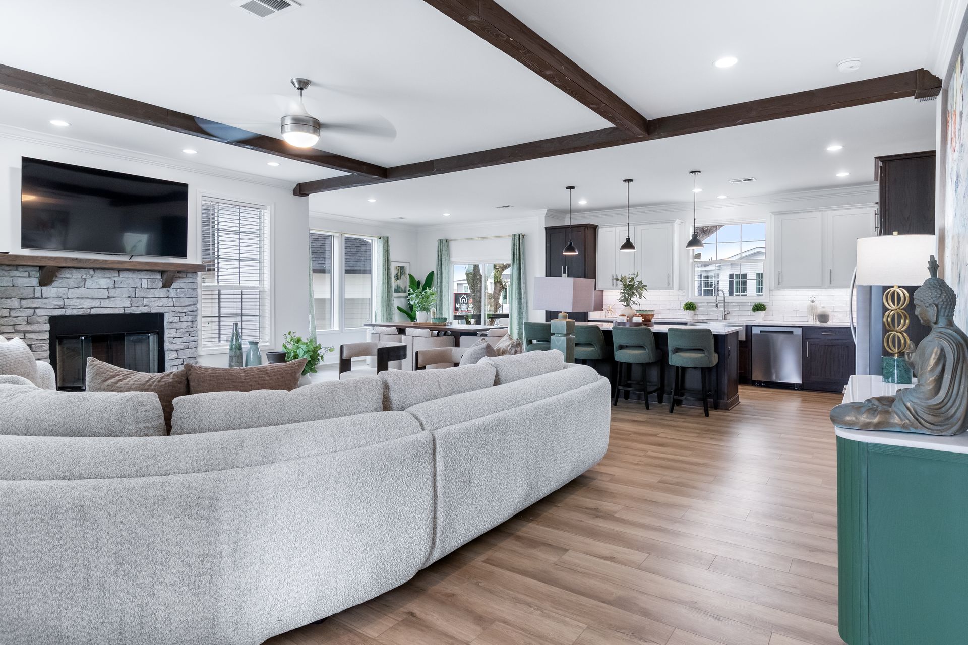 Modern open-concept living room with gray sectional, stone fireplace, and kitchen island with barstools