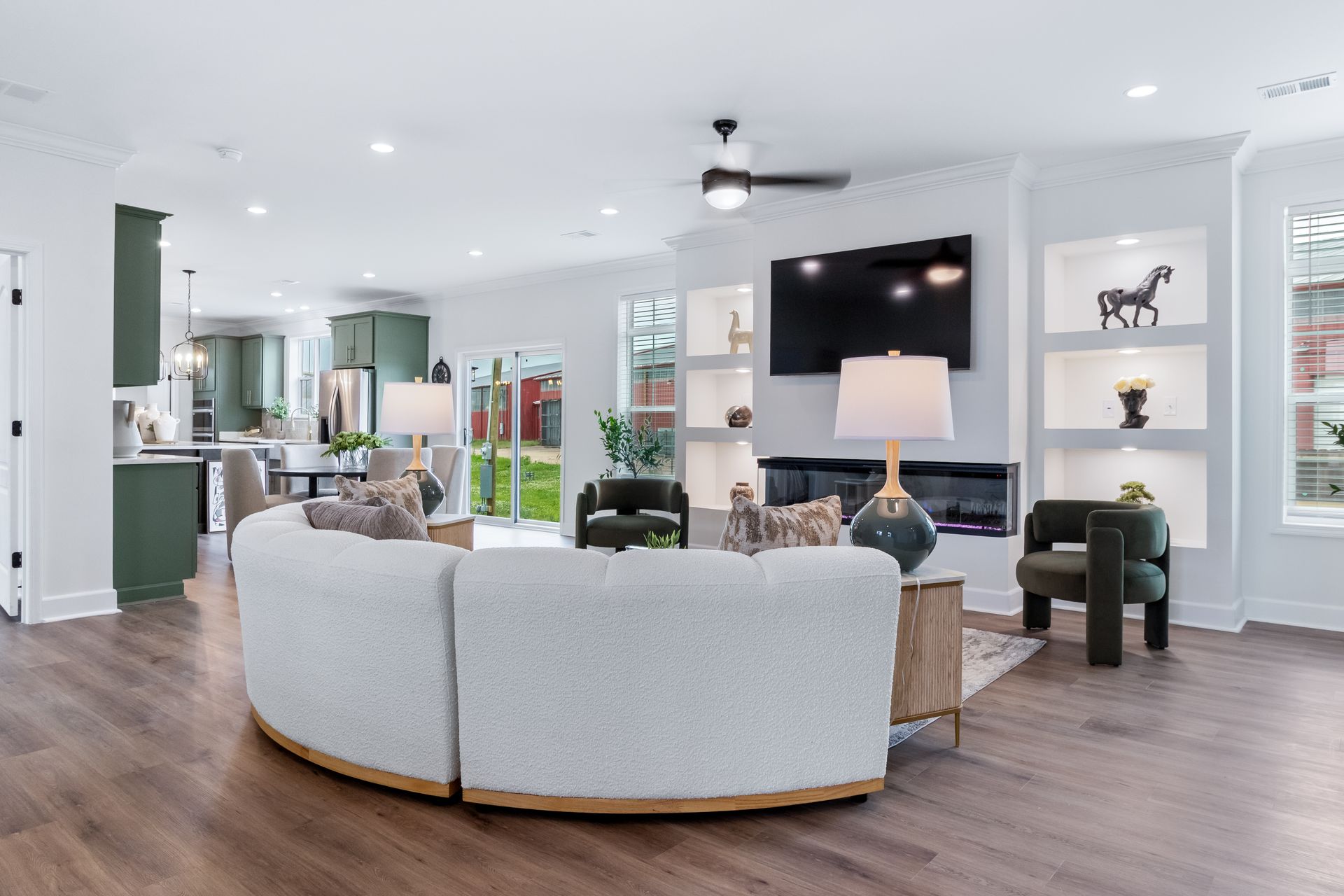 Bright open living room with a curved gray sofa, wall-mounted TV, and white shelves in a modern home