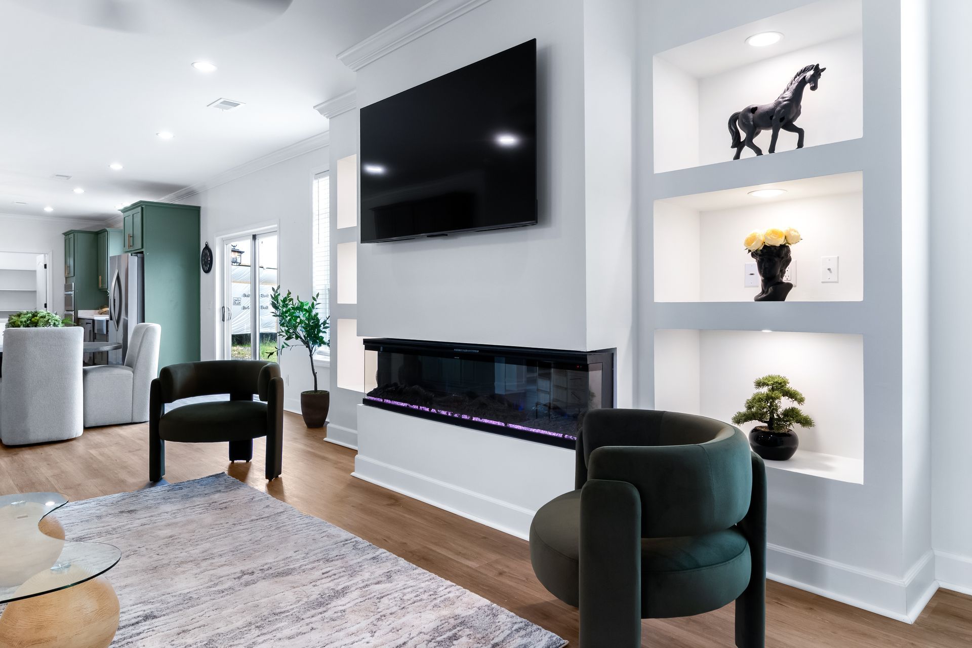 Modern living room with wall-mounted TV, fireplace, dark chairs, and built-in shelves with decor