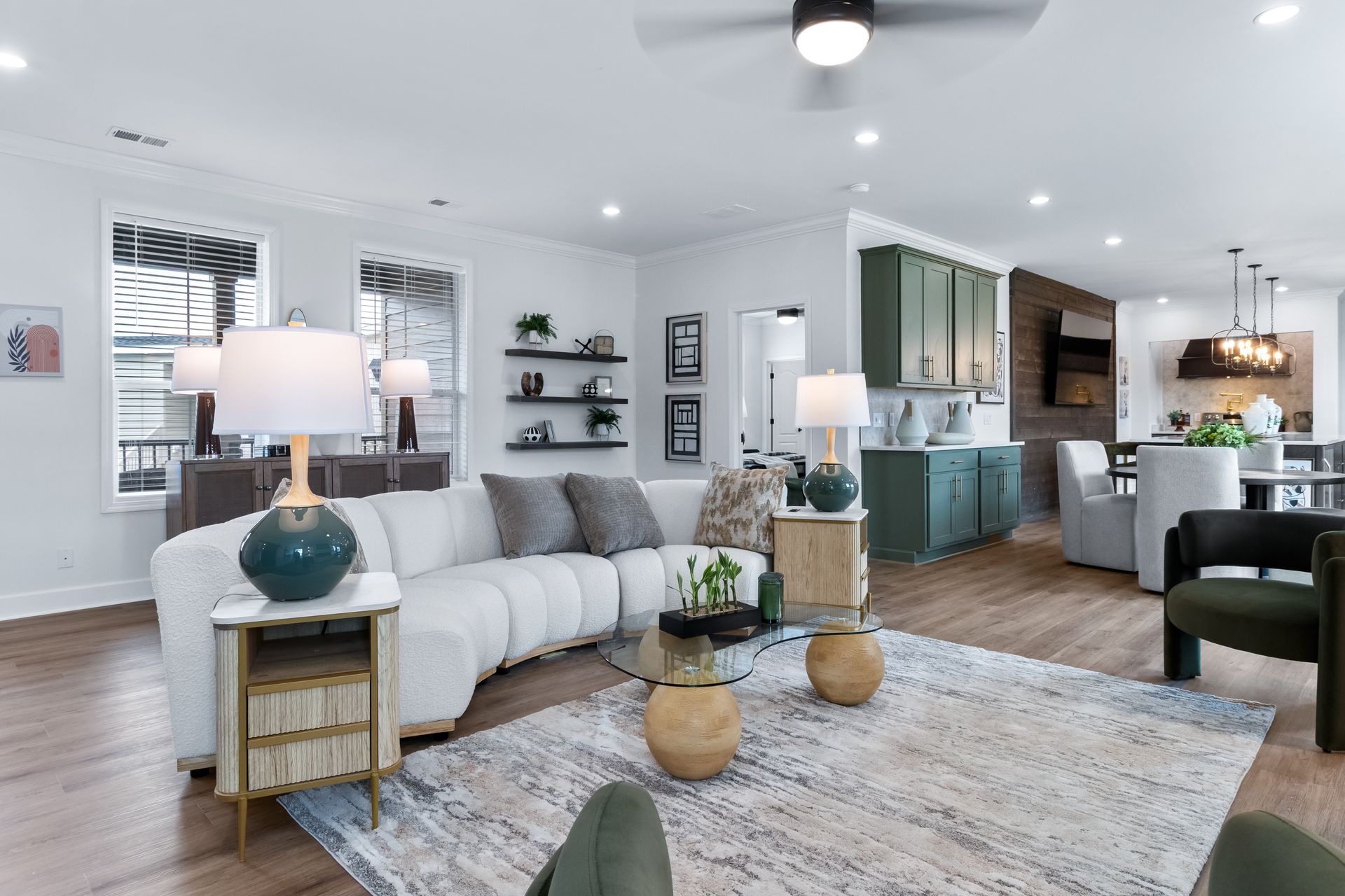 Bright modern open-plan living room with white sofa, wood accents, and kitchen in the background