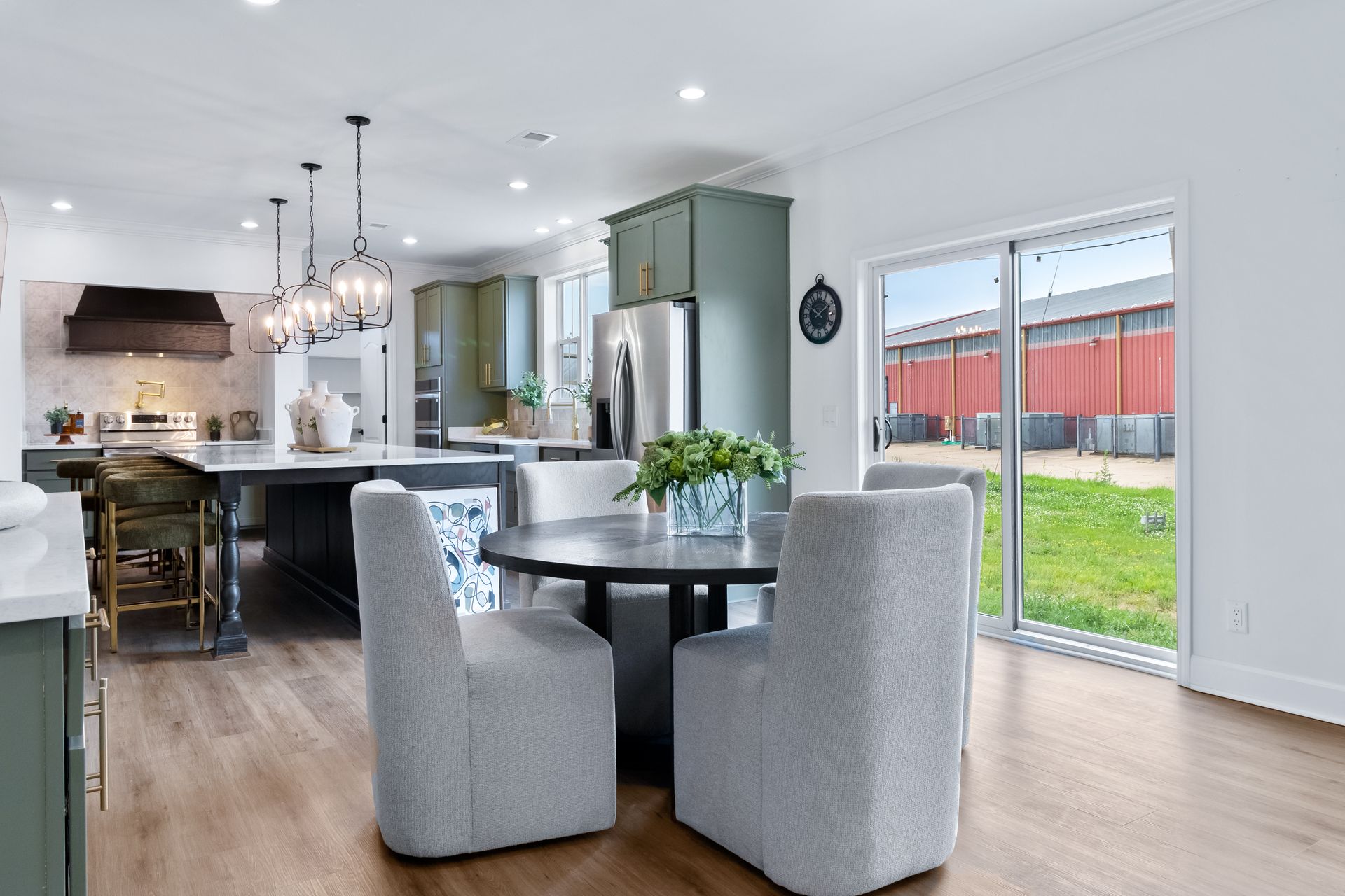 Open kitchen and dining area with gray chairs, island stools, and large windows overlooking a backyard