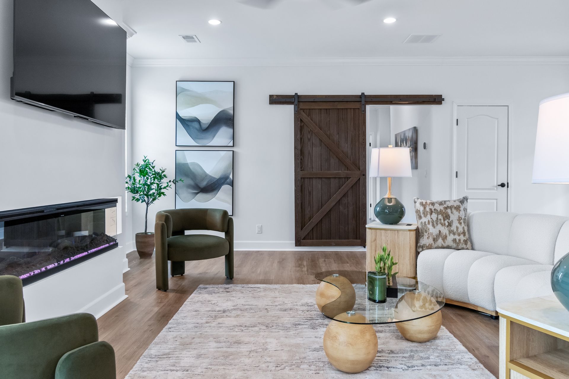 Bright modern living room with white sofa, fireplace, TV, wood floor, and barn door.