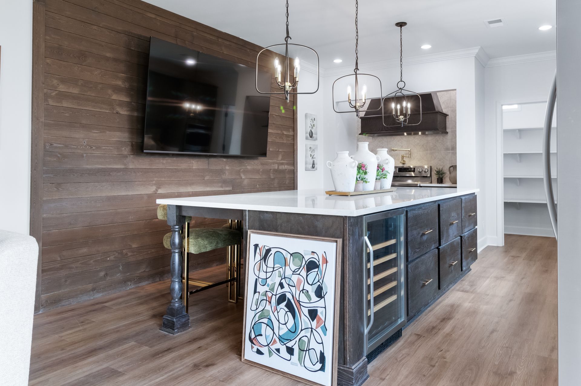 Modern kitchen with large island, wood floors, dark cabinets, and a wall-mounted TV