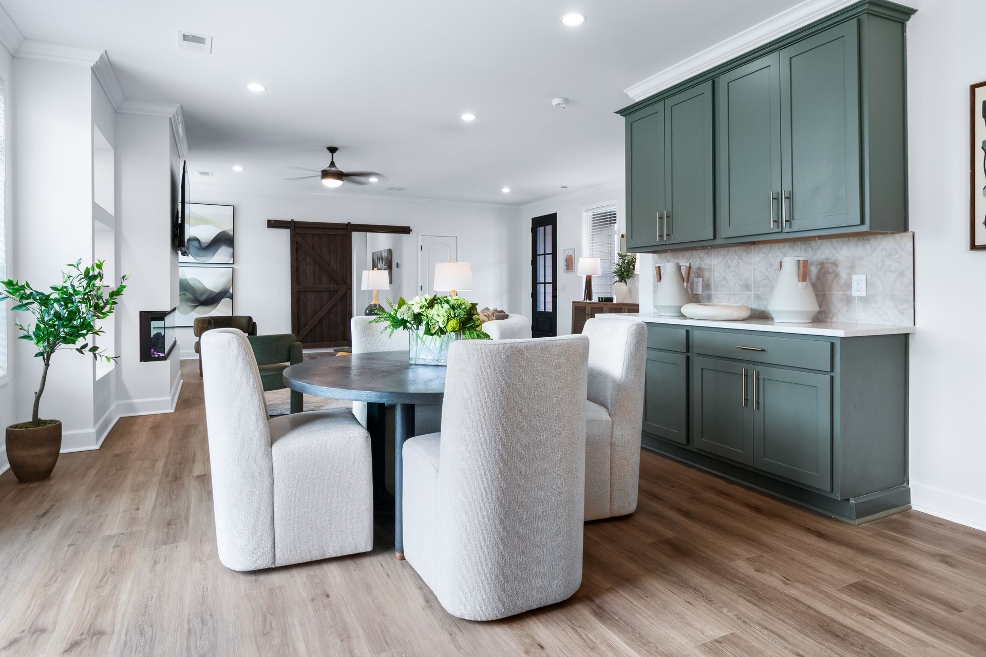 Bright open kitchen and dining area with green cabinets, white chairs, and wood floors