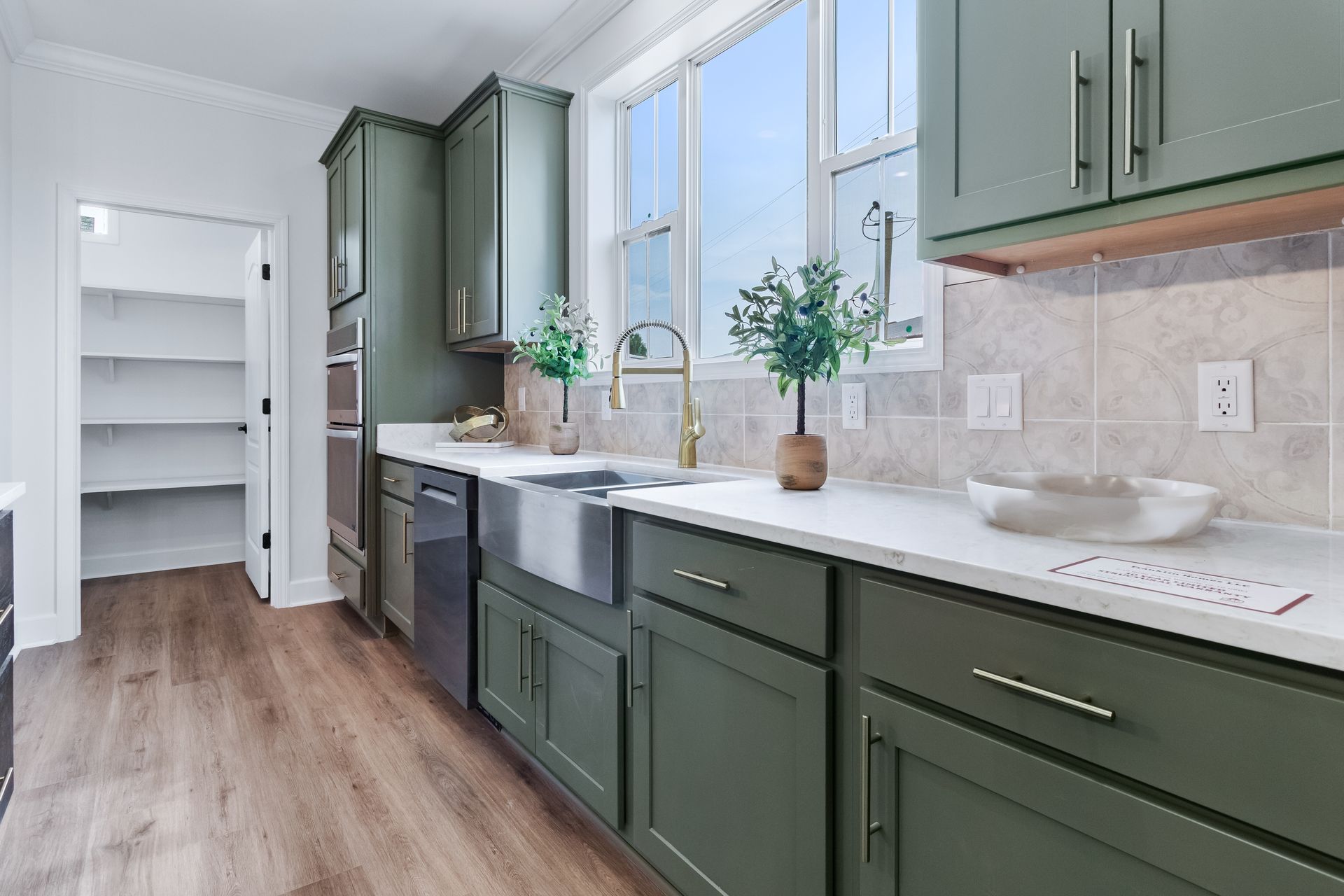 Bright kitchen with green cabinets, farmhouse sink, wood floors, and large windows.