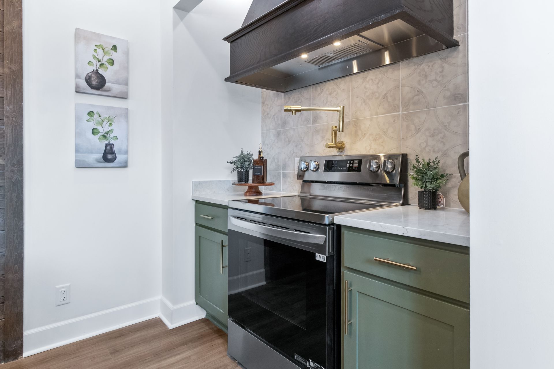 Modern kitchen with green cabinets, black stove, white countertops, and stainless range hood