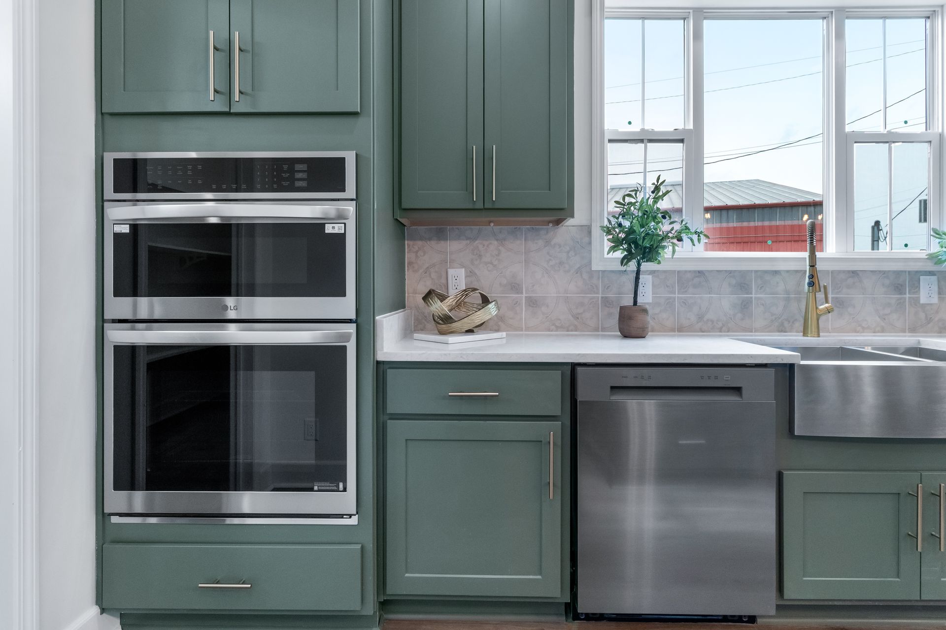 Modern kitchen with green cabinets, double oven, stainless dishwasher, and bright window over sink