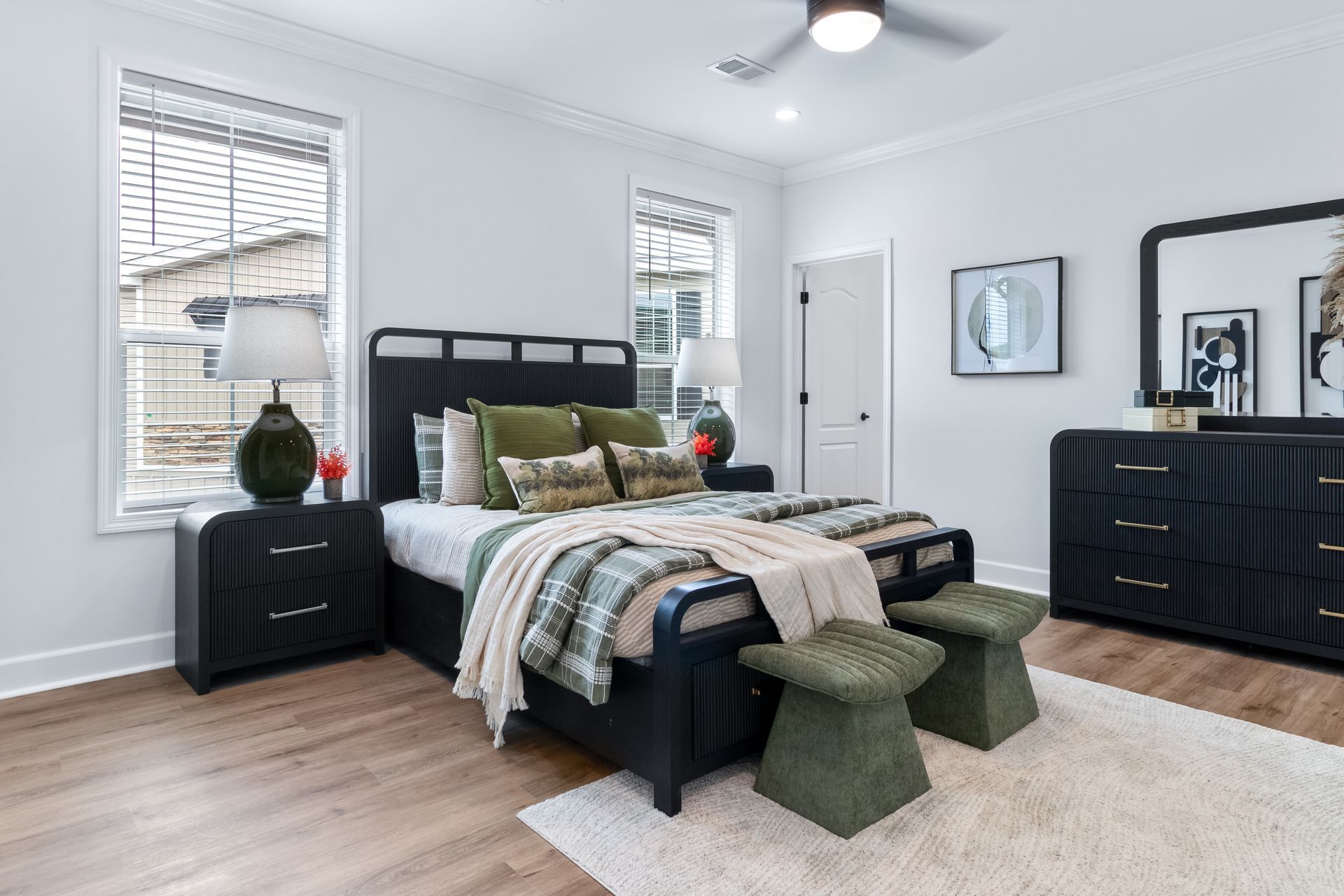 Bright modern bedroom with black bed, navy dressers, green pillows, and light wood floors