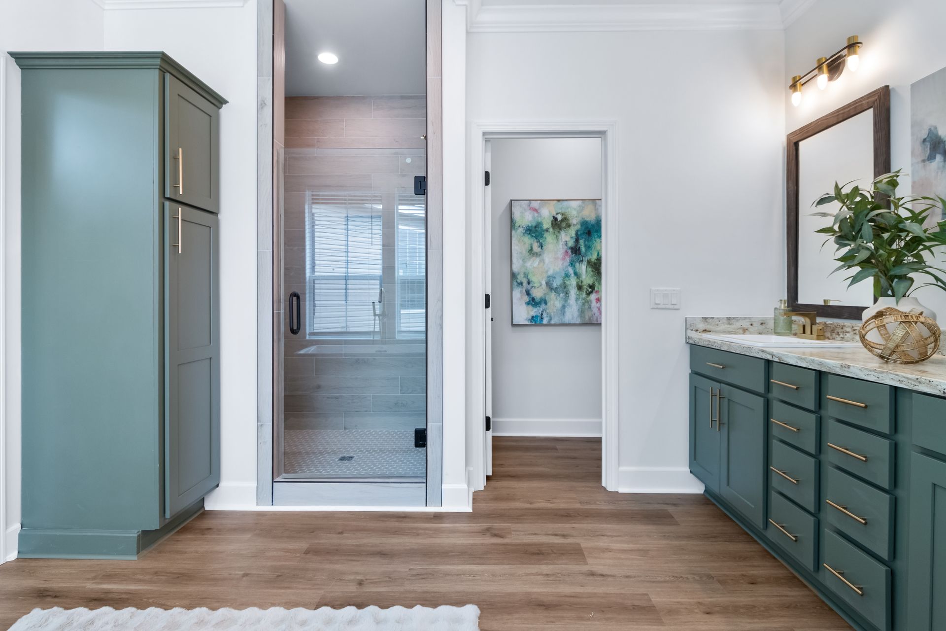 Spacious bathroom with teal cabinets, white walls, wood floor, shower, and vanity mirror.