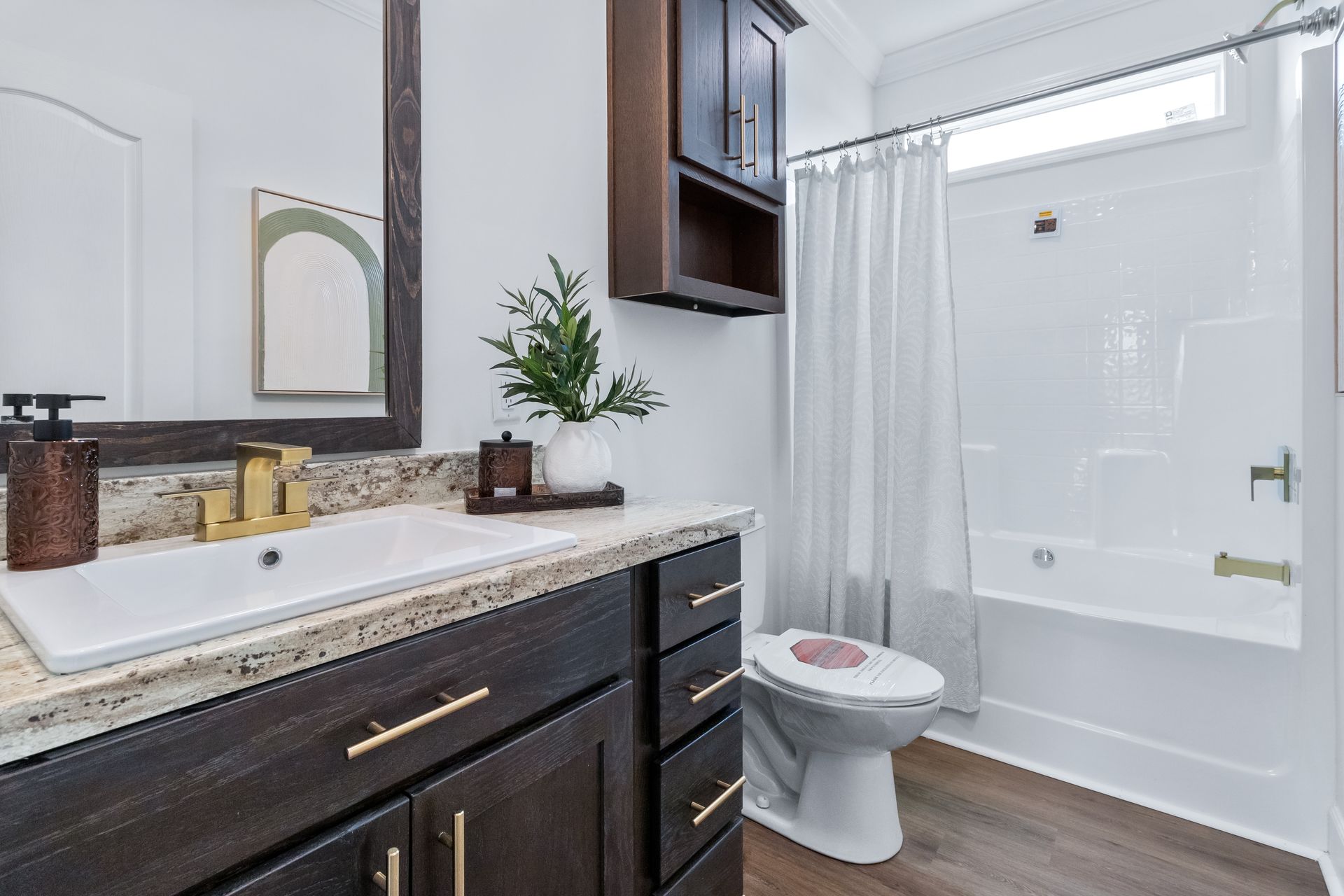Modern bathroom with dark vanity, white sink, mirror, toilet, and shower tub behind a curtain.