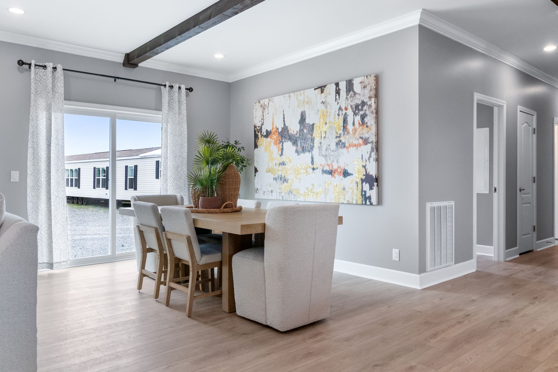 Bright dining area with wood table, beige chairs, large abstract wall art, and sliding glass doors to a balcony.