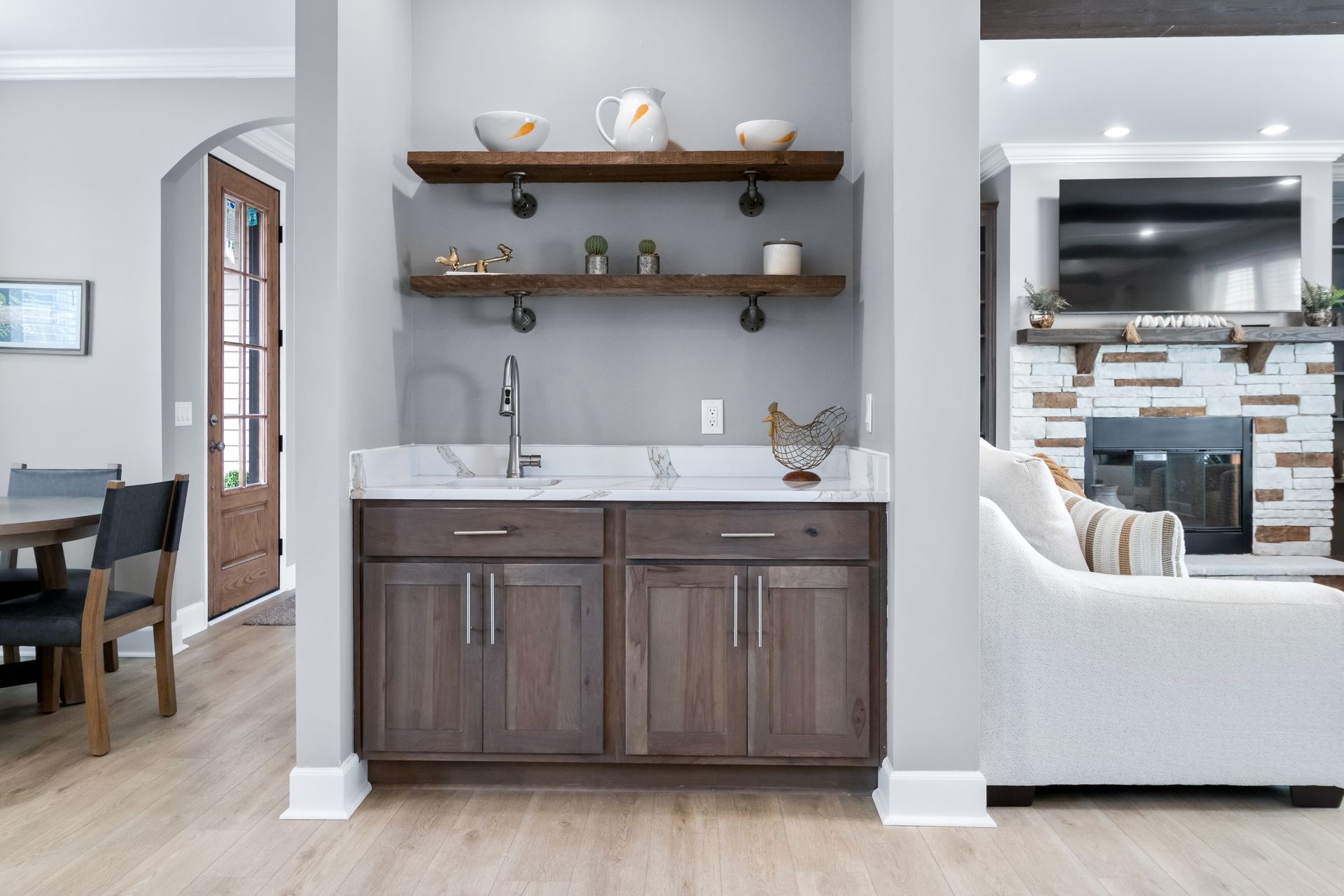 Open kitchen nook with wood cabinets, white countertop, and floating shelves in a bright home interior