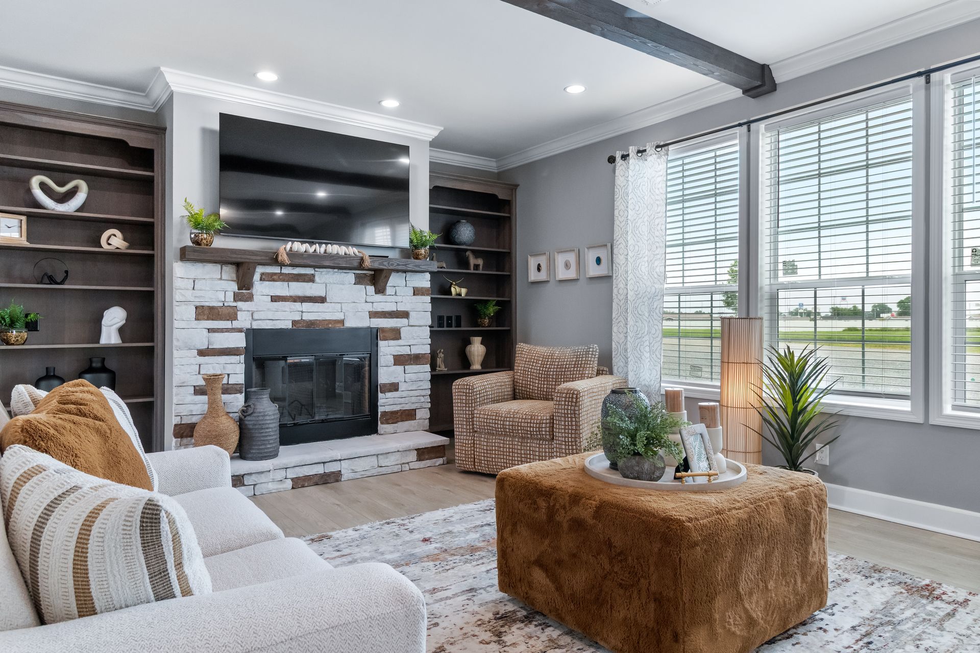 Modern living room with gray walls, stone fireplace, patterned rug, and large windows with blinds