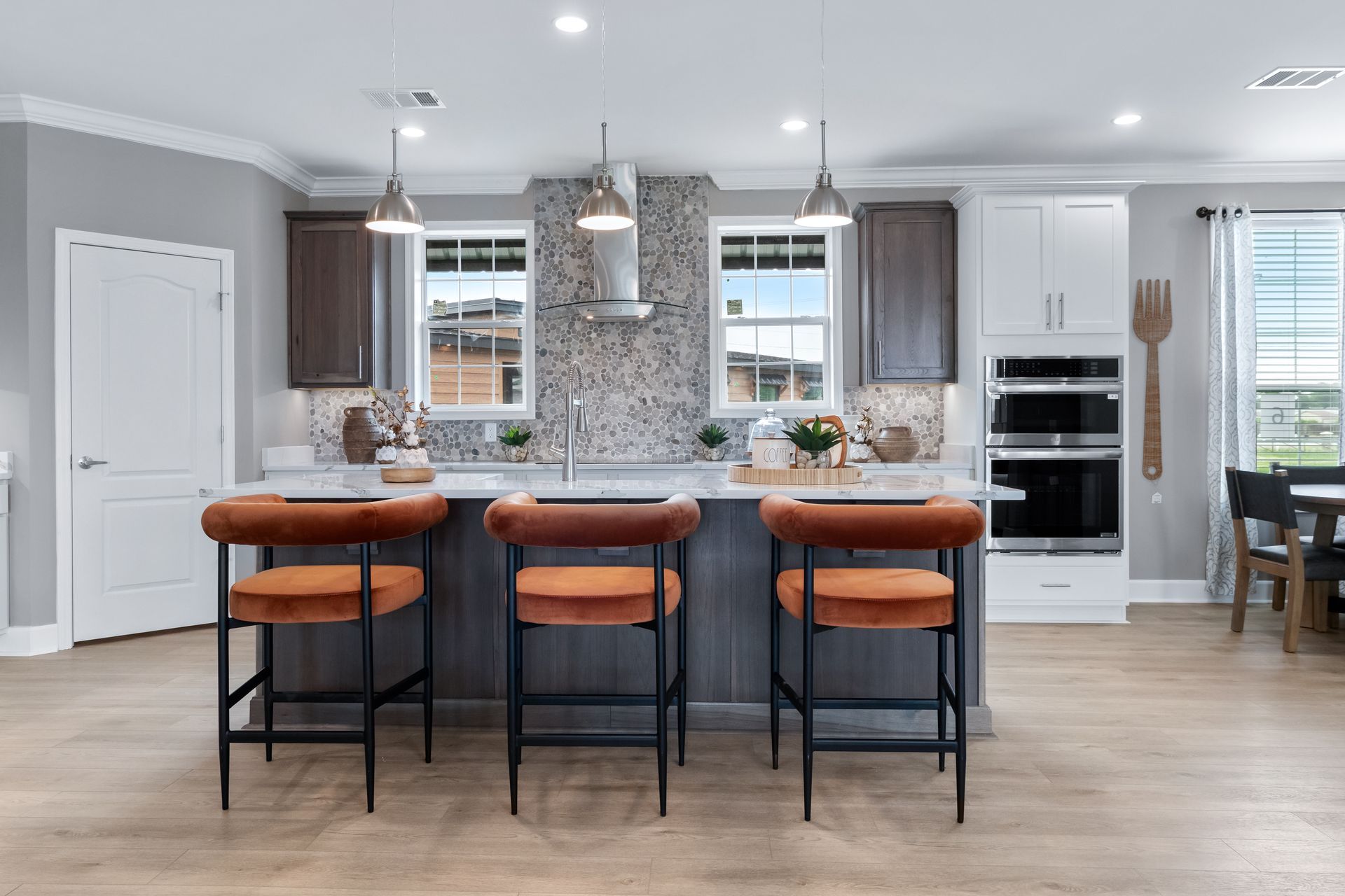 Modern kitchen with white cabinets, gray island, three brown barstools, and pendant lights